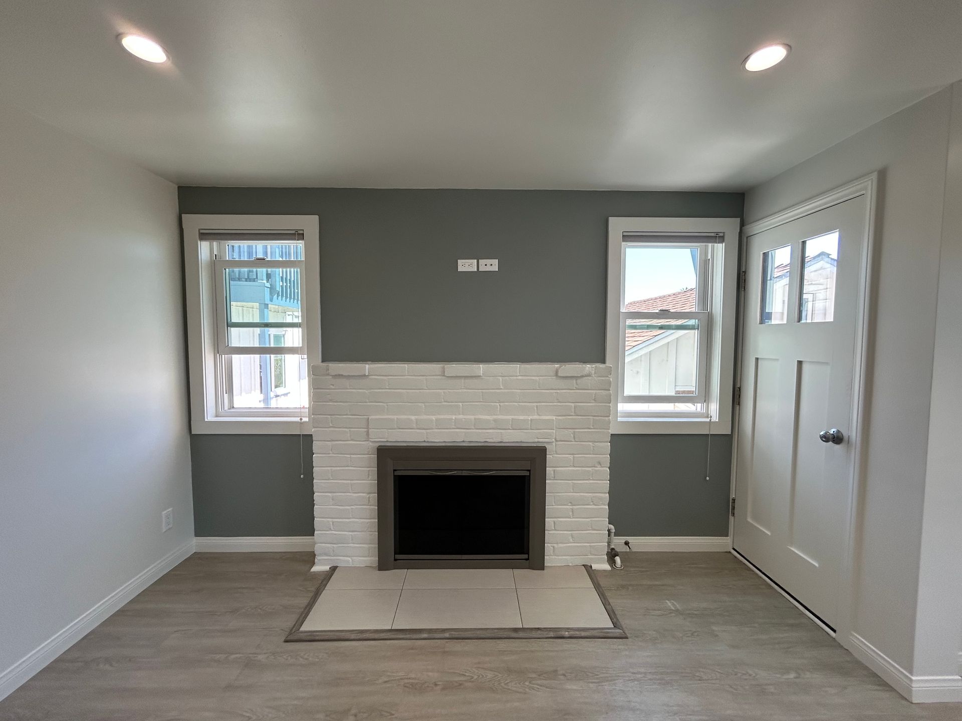 Empty living room with a white fireplace, two windows, and a door on the right.