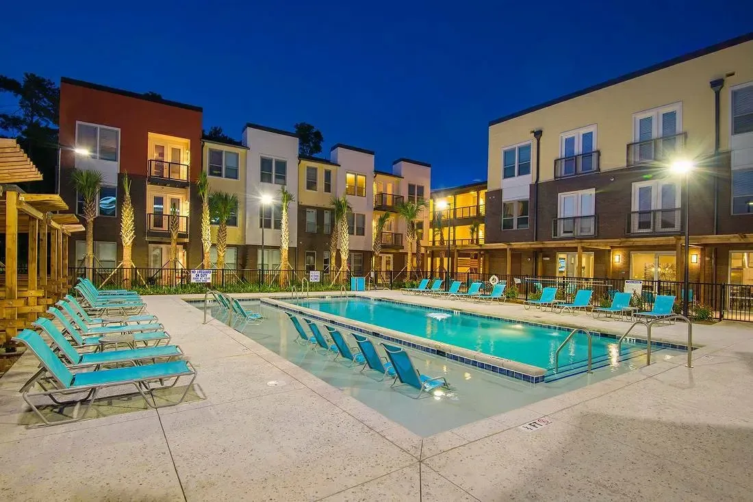 Modern apartment building with a large outdoor swimming pool and lounge chairs.