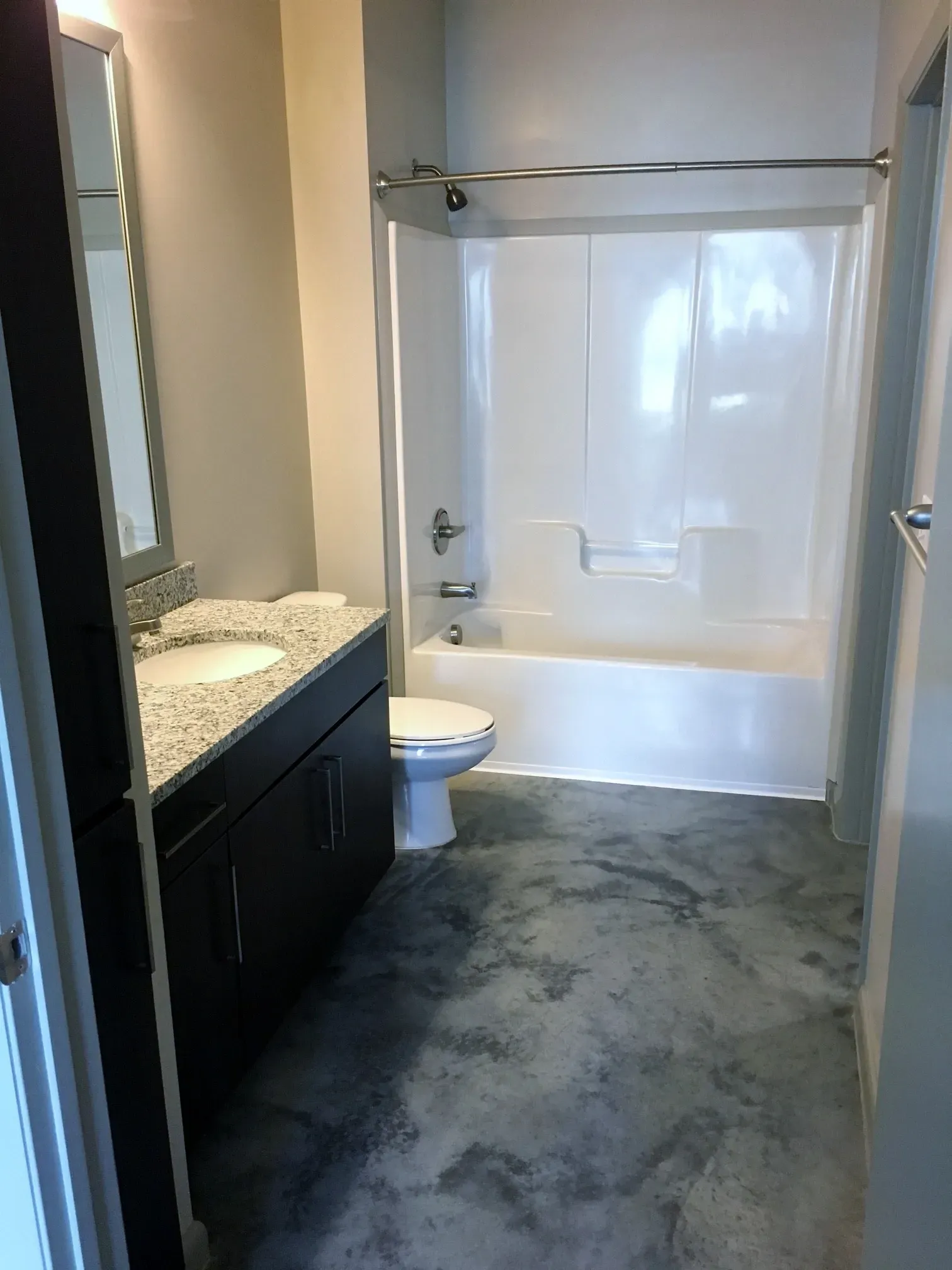 Modern bathroom with a granite countertop vanity, dark wood cabinets, a toilet, and a white bathtub/shower combo.