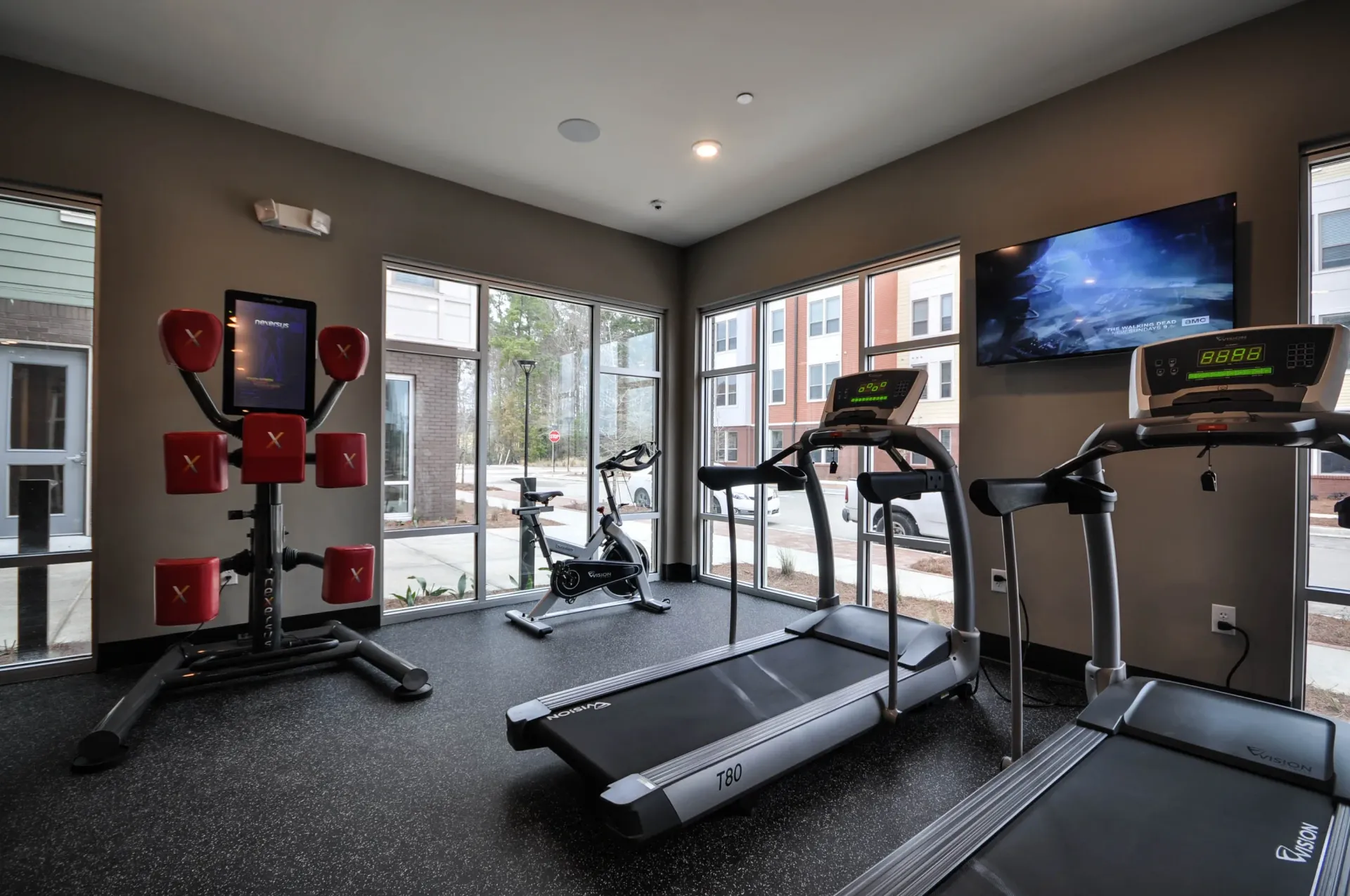 Treadmills, stationary bike, and punching station in a well-lit fitness center with large windows.