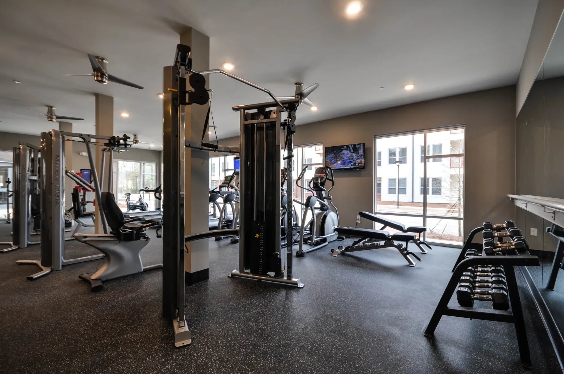Modern apartment gym with weight machines, treadmills, and dumbbells.
