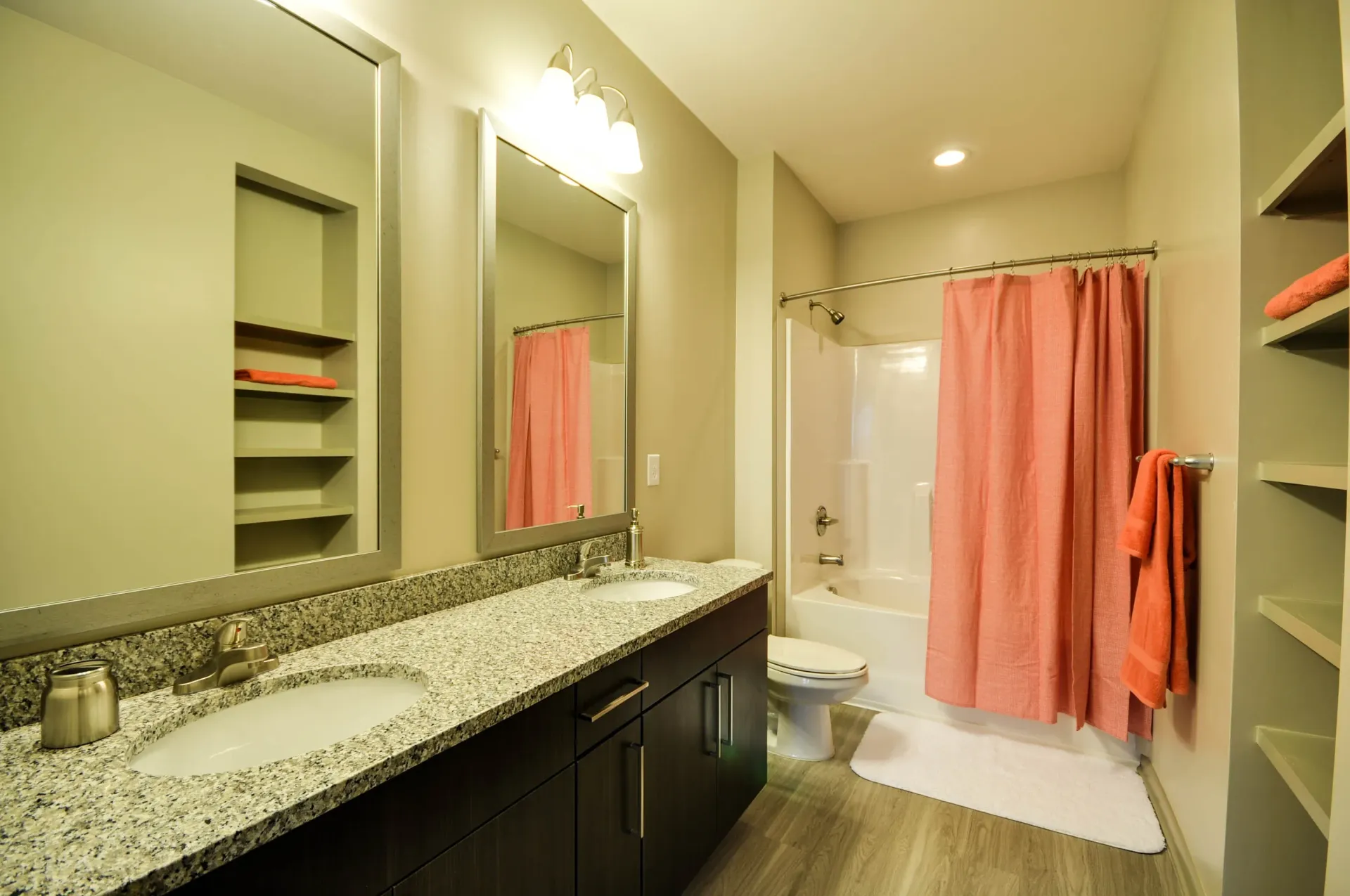 Double vanity with granite countertop and modern fixtures, adjacent to a bathtub with a coral shower curtain.