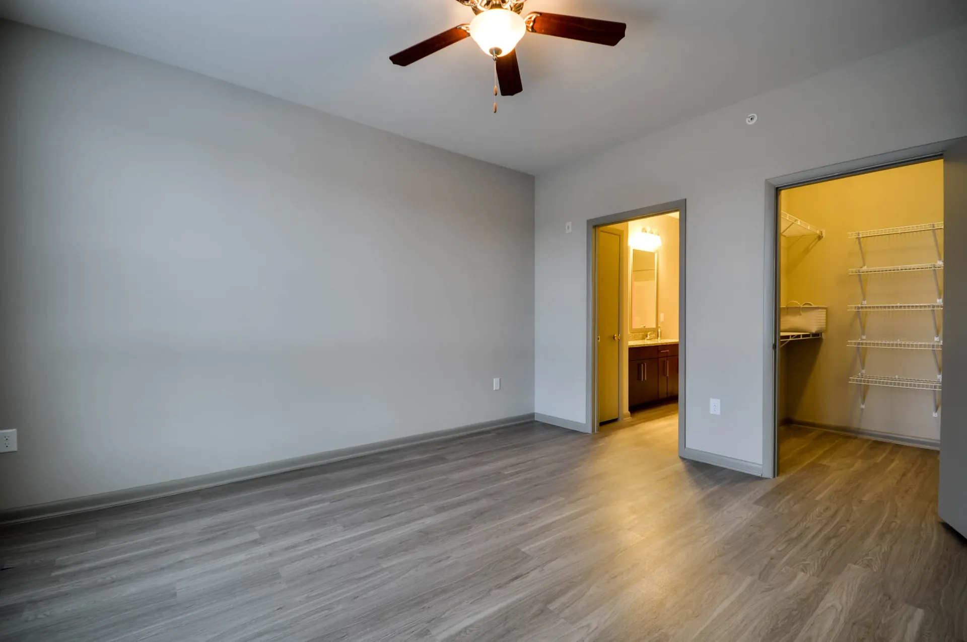Empty apartment bedroom with a ceiling fan, closet, and bathroom entrance.