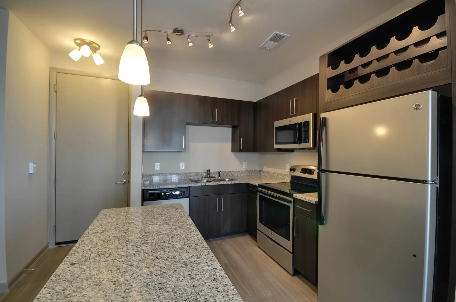 Modern kitchen with dark wood cabinets, granite countertops, stainless steel appliances, and a large island.