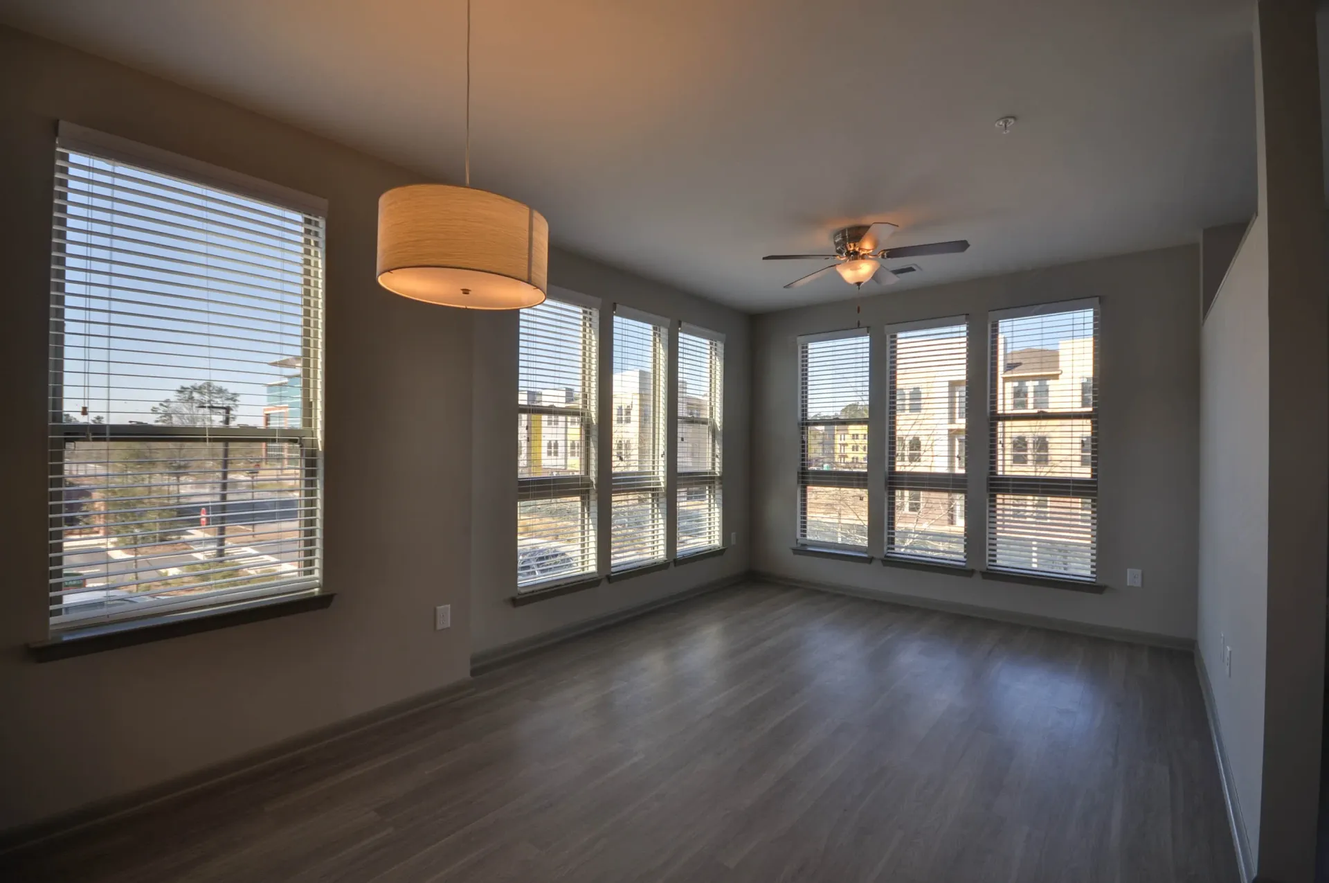 Empty living room with large windows and a ceiling fan.