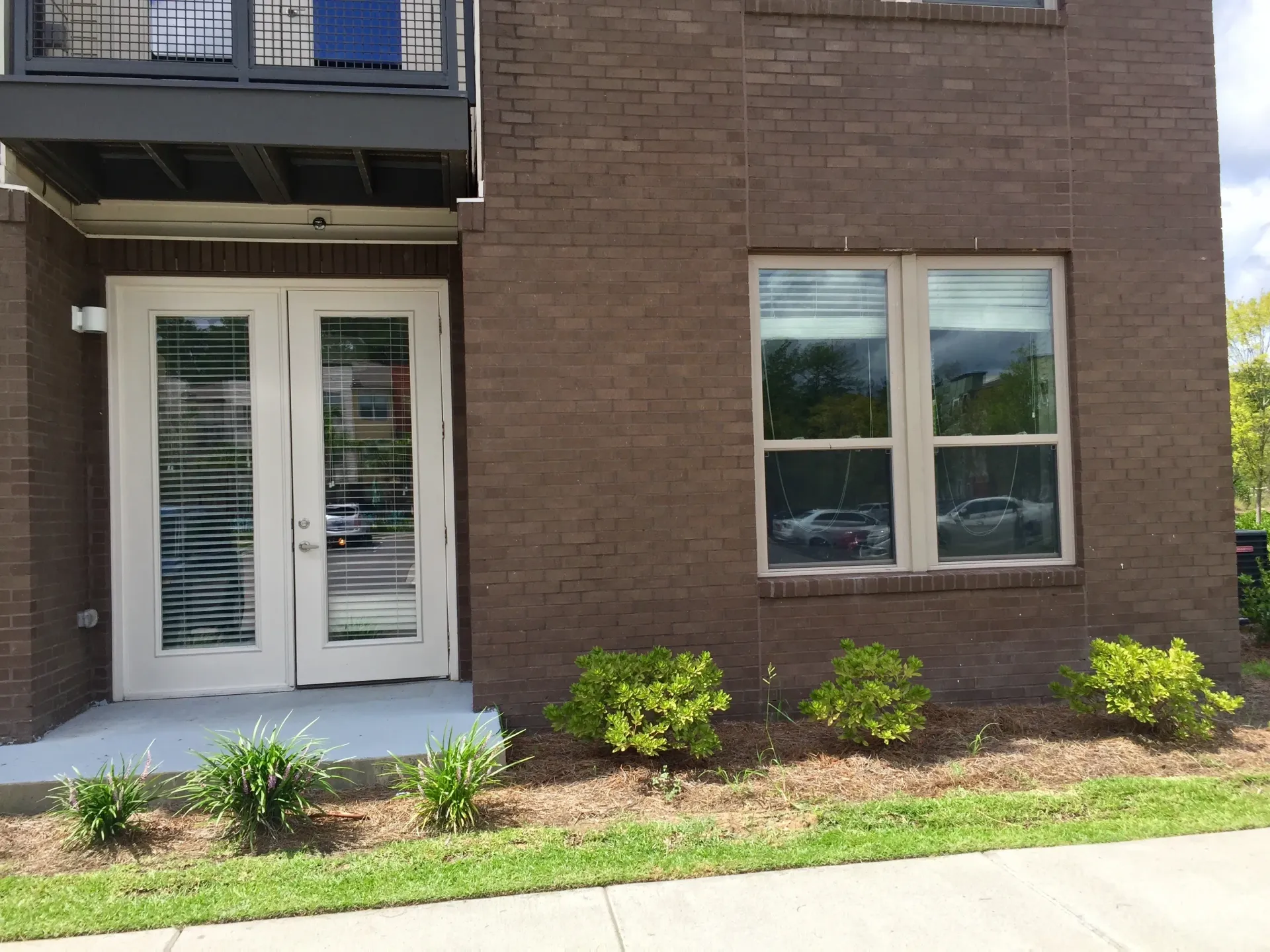 Exterior view of a brick building with double doors and a window showing car reflections.