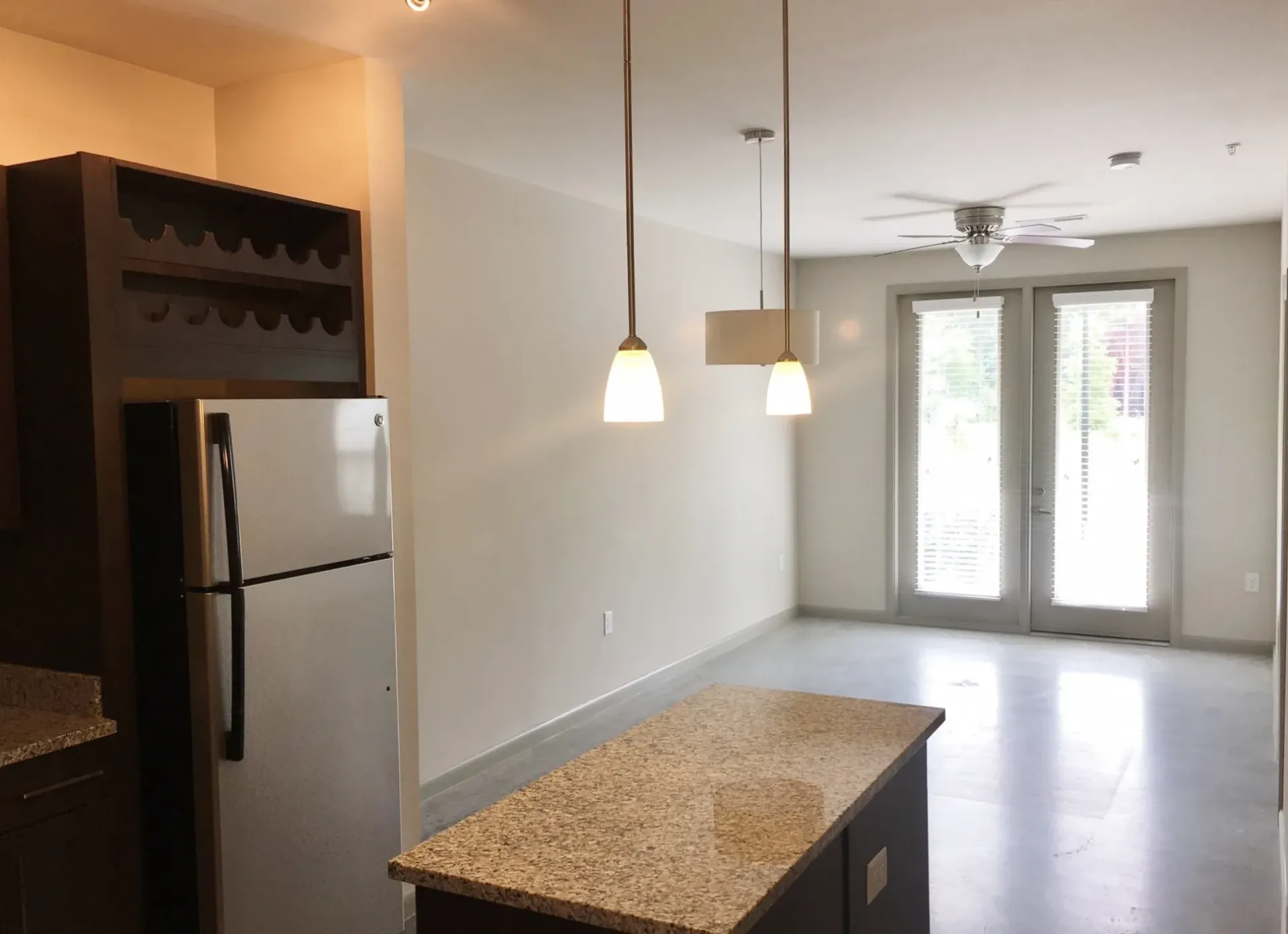 Kitchen island with granite countertop, stainless steel refrigerator, and dining area with ceiling fan and double doors.