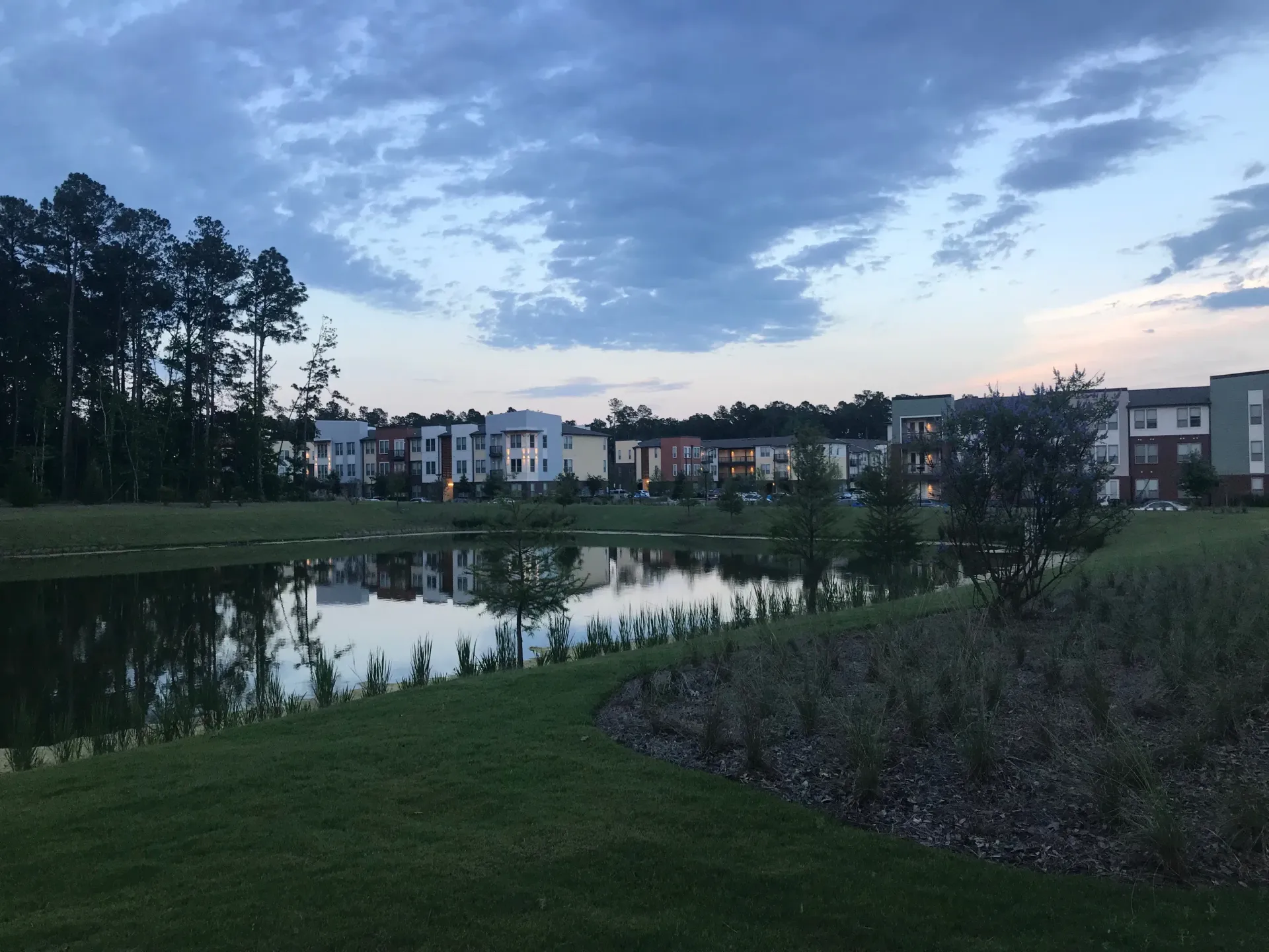 Exterior view of apartment buildings reflected in a pond at dusk.