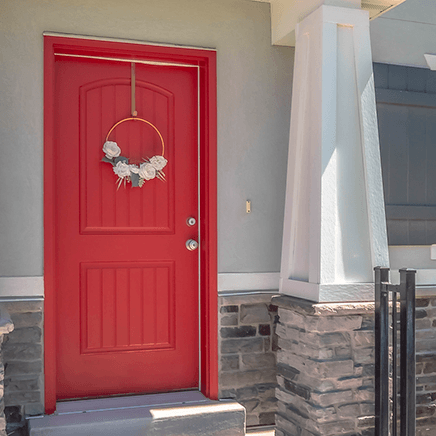 Red front door with a white floral wreath beside a stone porch column.
