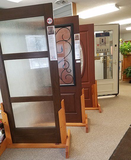 Door Selection Interior showroom with several wooden entry doors on display, including a dark door with frosted glass panels.