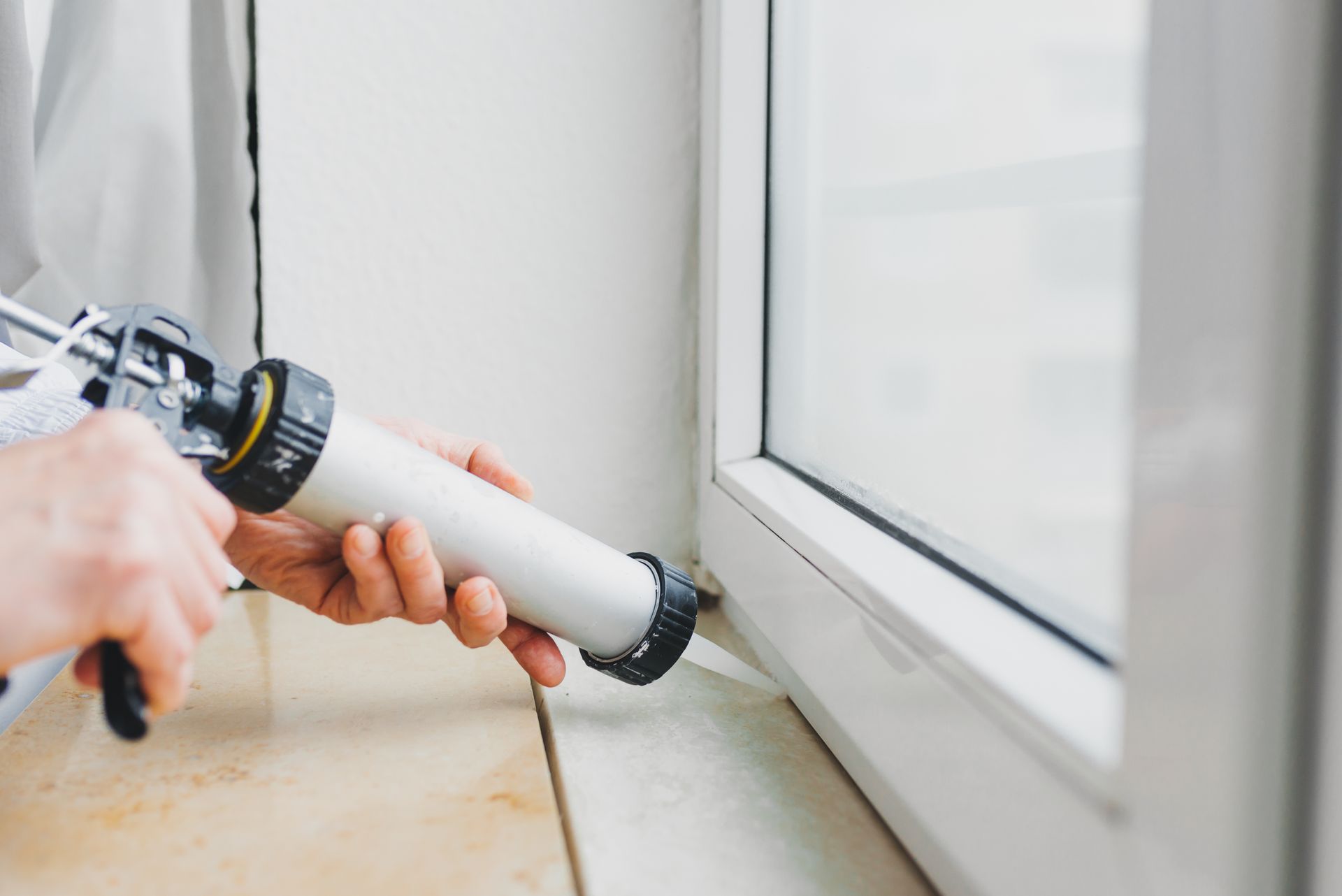 Personne appliquant du mastic blanc sur un cadre de fenêtre.