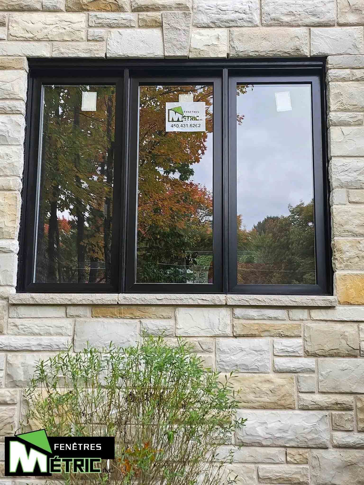 Trois fenêtres noires à cadre installées dans un mur de pierre avec logo d'entreprise visible.