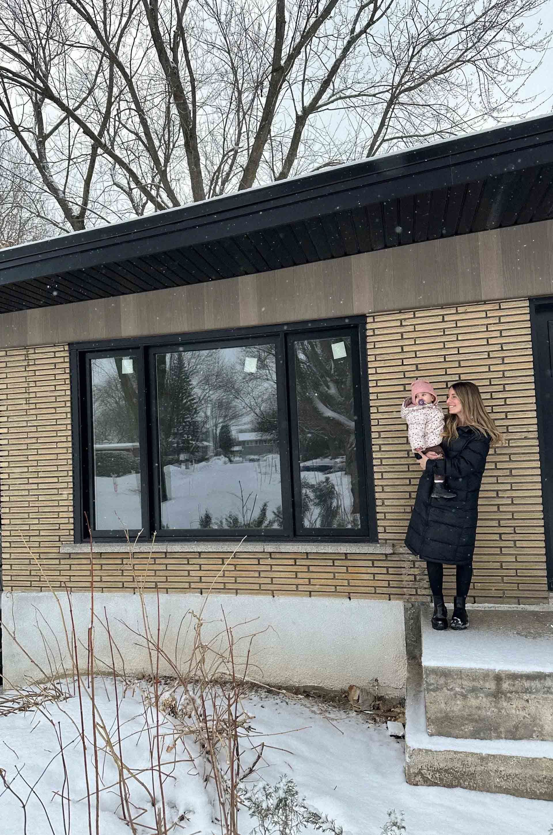 Femme tenant un b&eacute;b&eacute; devant une fen&ecirc;tre &agrave; trois carreaux d'une maison moderne en hiver.