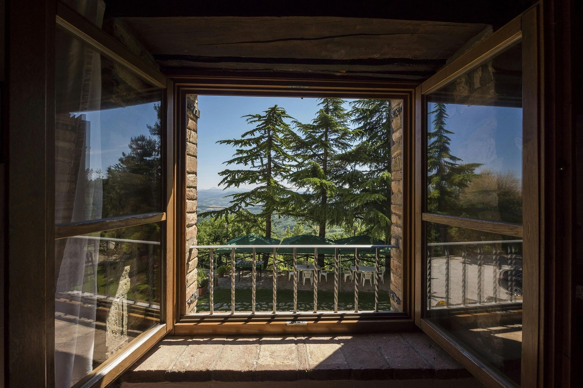 Fenêtre ouverte encadrant une vue sur des arbres verts et un ciel bleu.