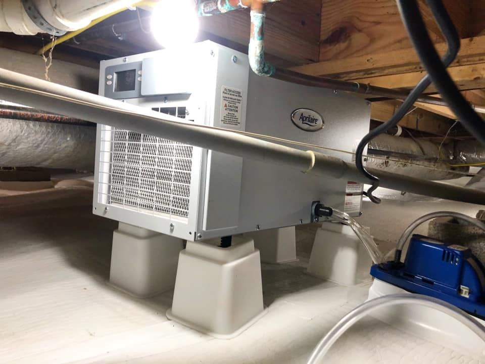 A humidifier is sitting under a ceiling in a basement.