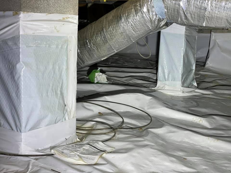 A crawl space covered in plastic and ducts with a light on the floor.