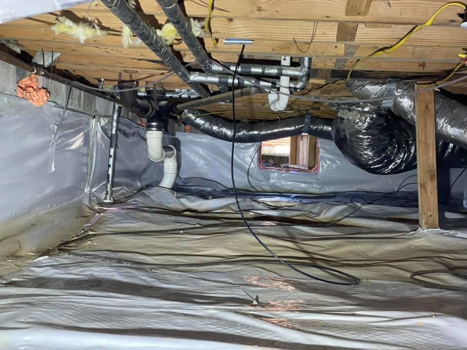 Two men are crawling under a house in a basement.