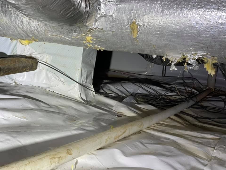 A crawl space with a lot of pipes and wires coming out of it.