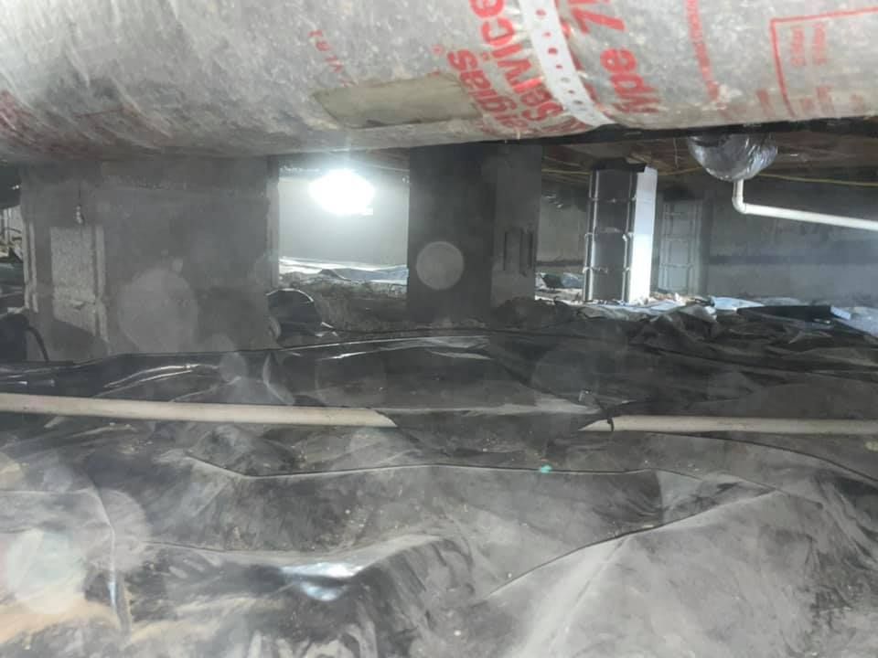 A dirty basement with a large piece of insulation hanging from the ceiling.