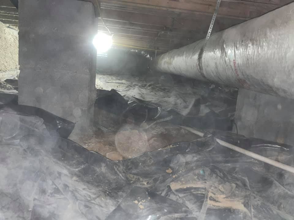 A dirty basement with a lot of pipes and smoke coming out of it.