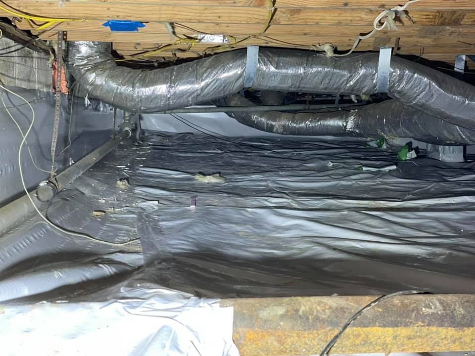 A crawl space with a lot of pipes and wires coming out of it.