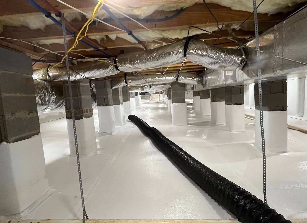 A crawl space with a lot of pipes hanging from the ceiling.