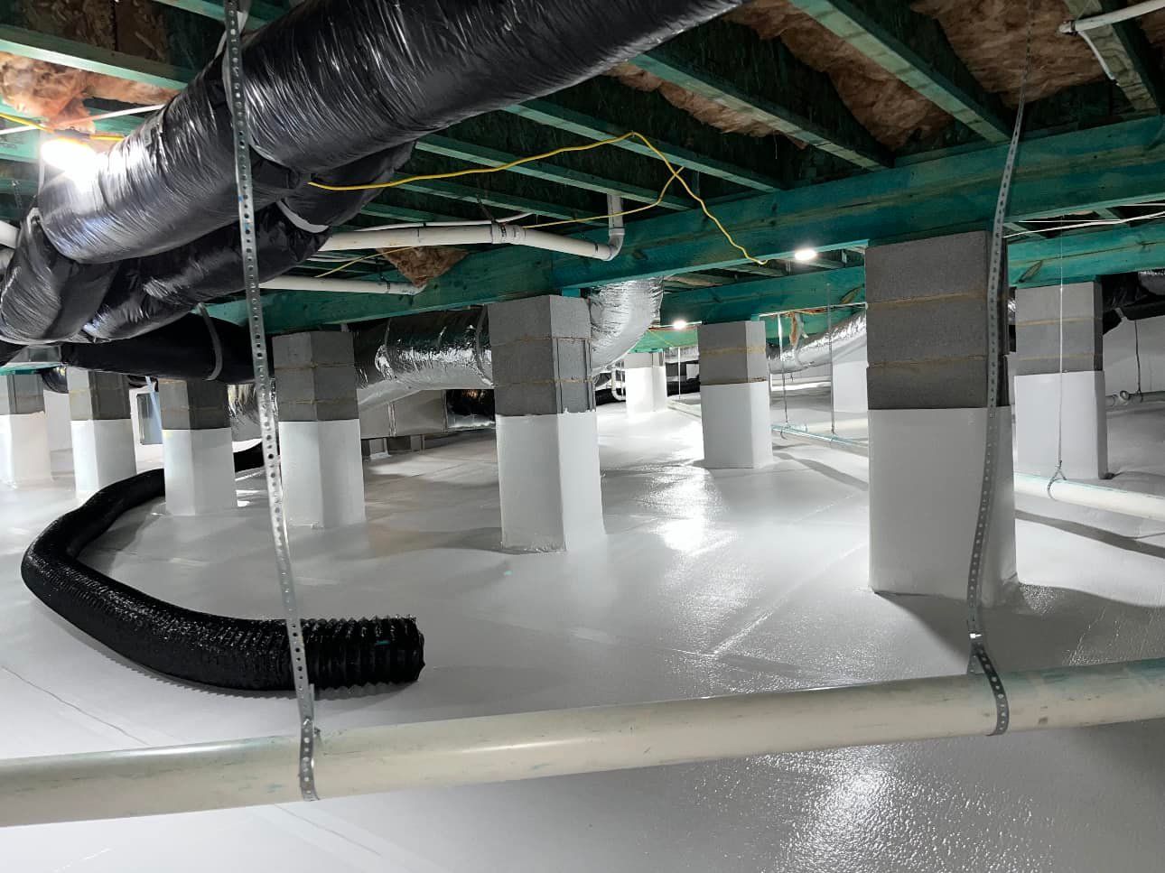 A crawl space with a lot of pipes hanging from the ceiling.