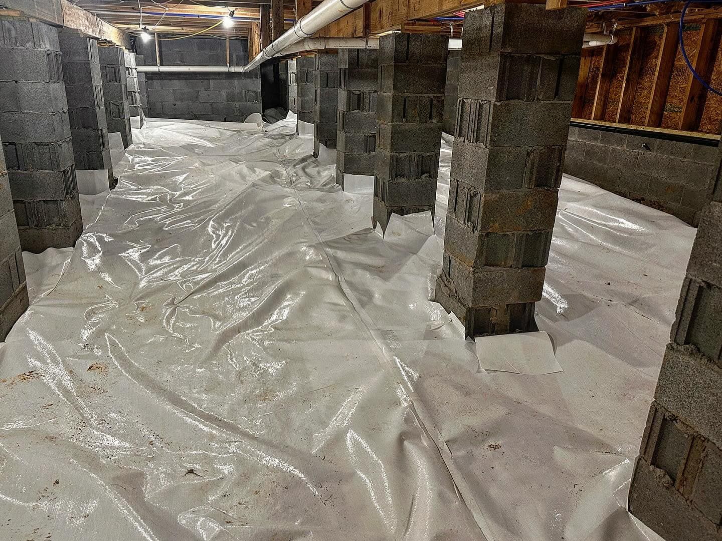 A basement with a lot of plastic covering the floor and pillars.
