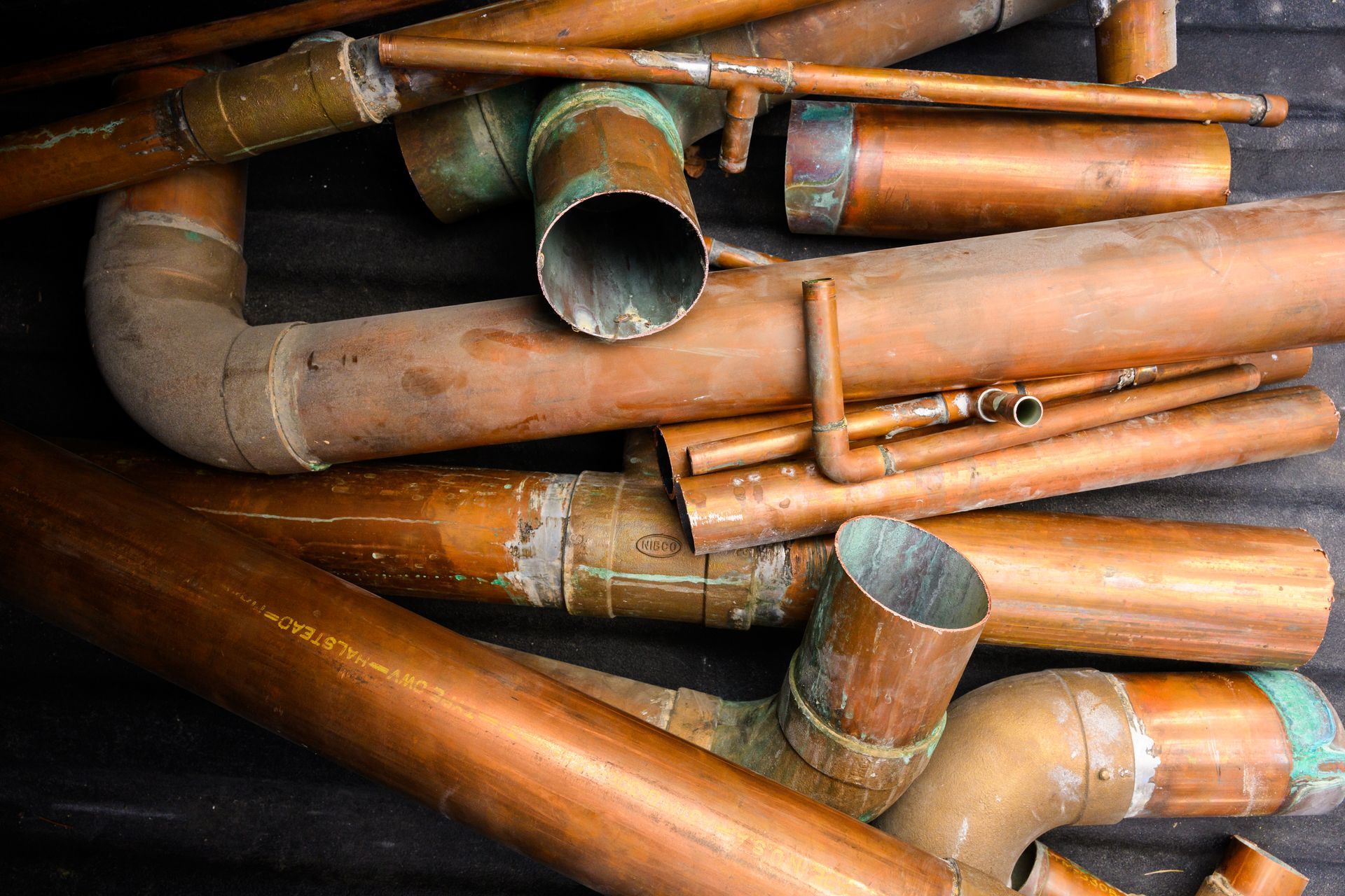 A collection of copper pipes and fittings of varying sizes and angles, arranged randomly.