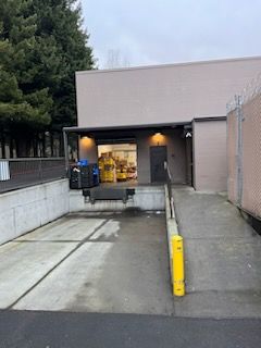 Loading dock with a ramp, gray building, and yellow bollards.