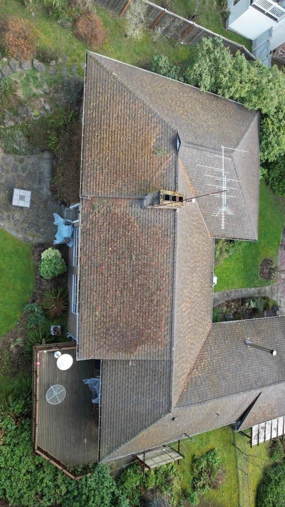 Overhead view of a house with brown roof, deck, surrounded by green grass and trees.