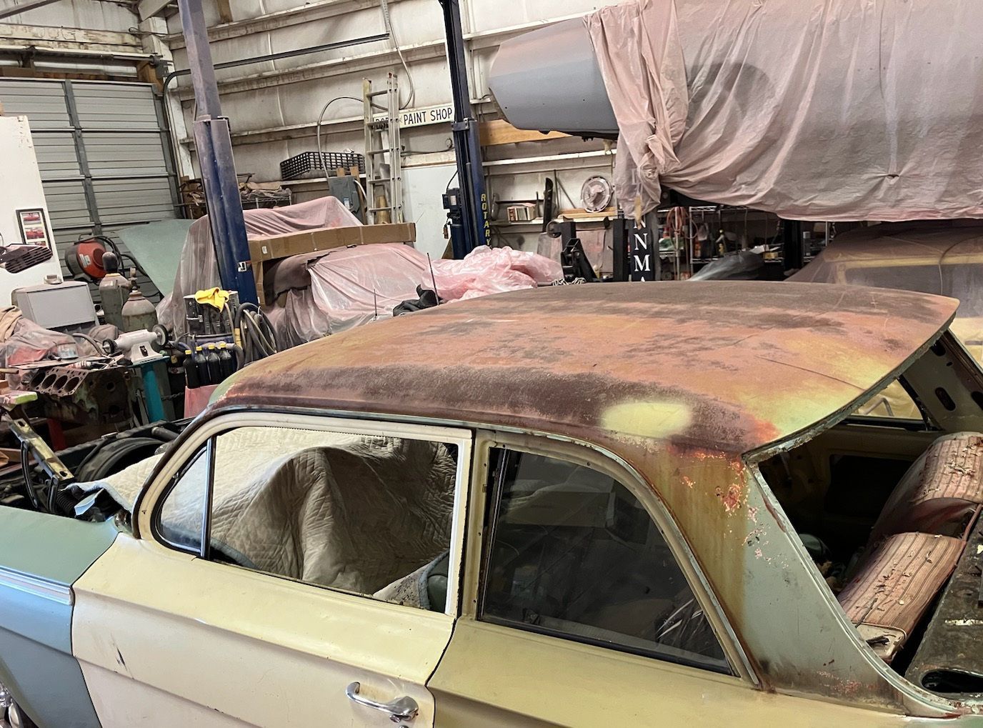 Vintage car in a workshop, roof rusted, with green and yellow paint.