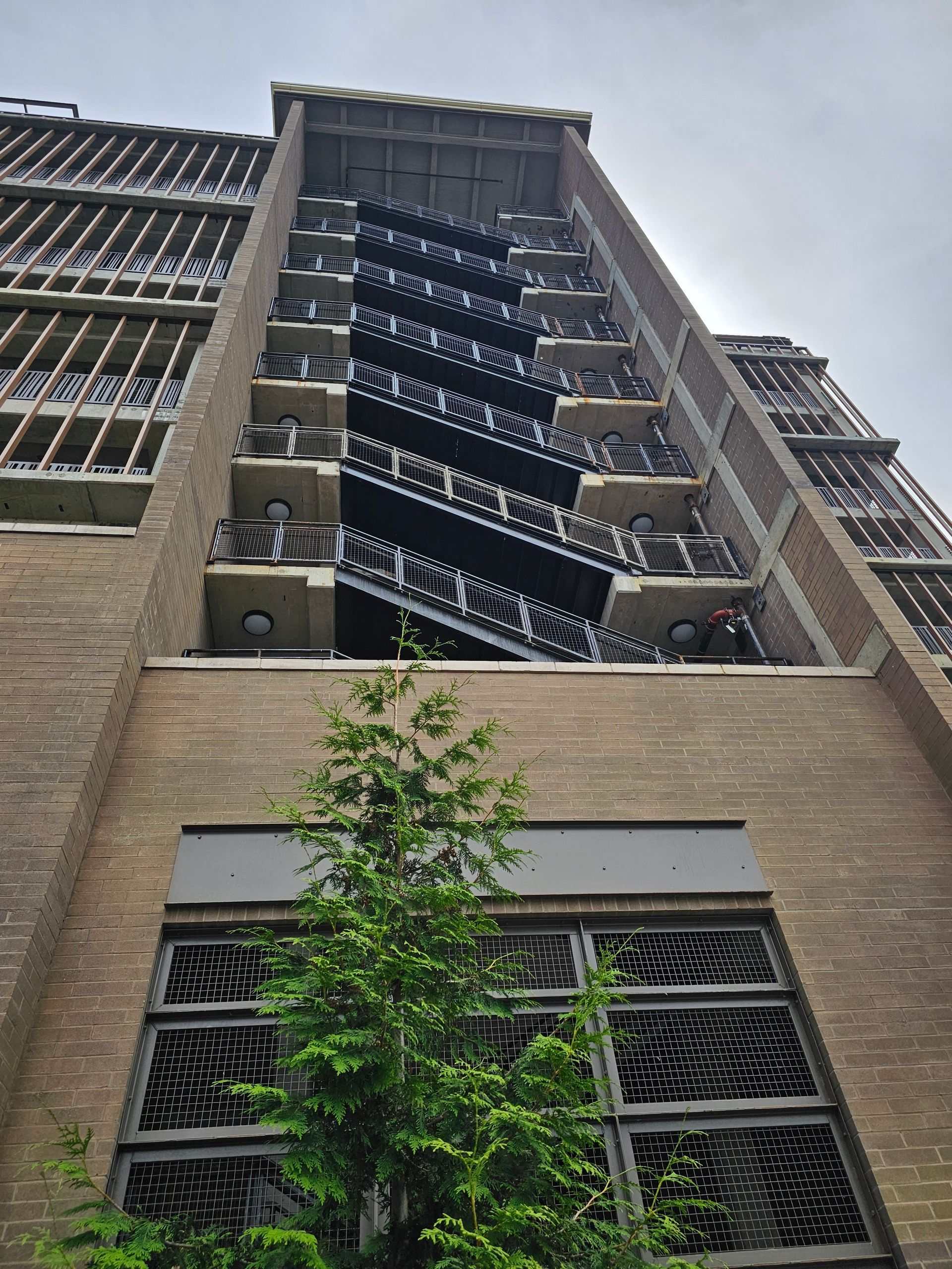 Brick building with exterior fire escape and small tree in front.