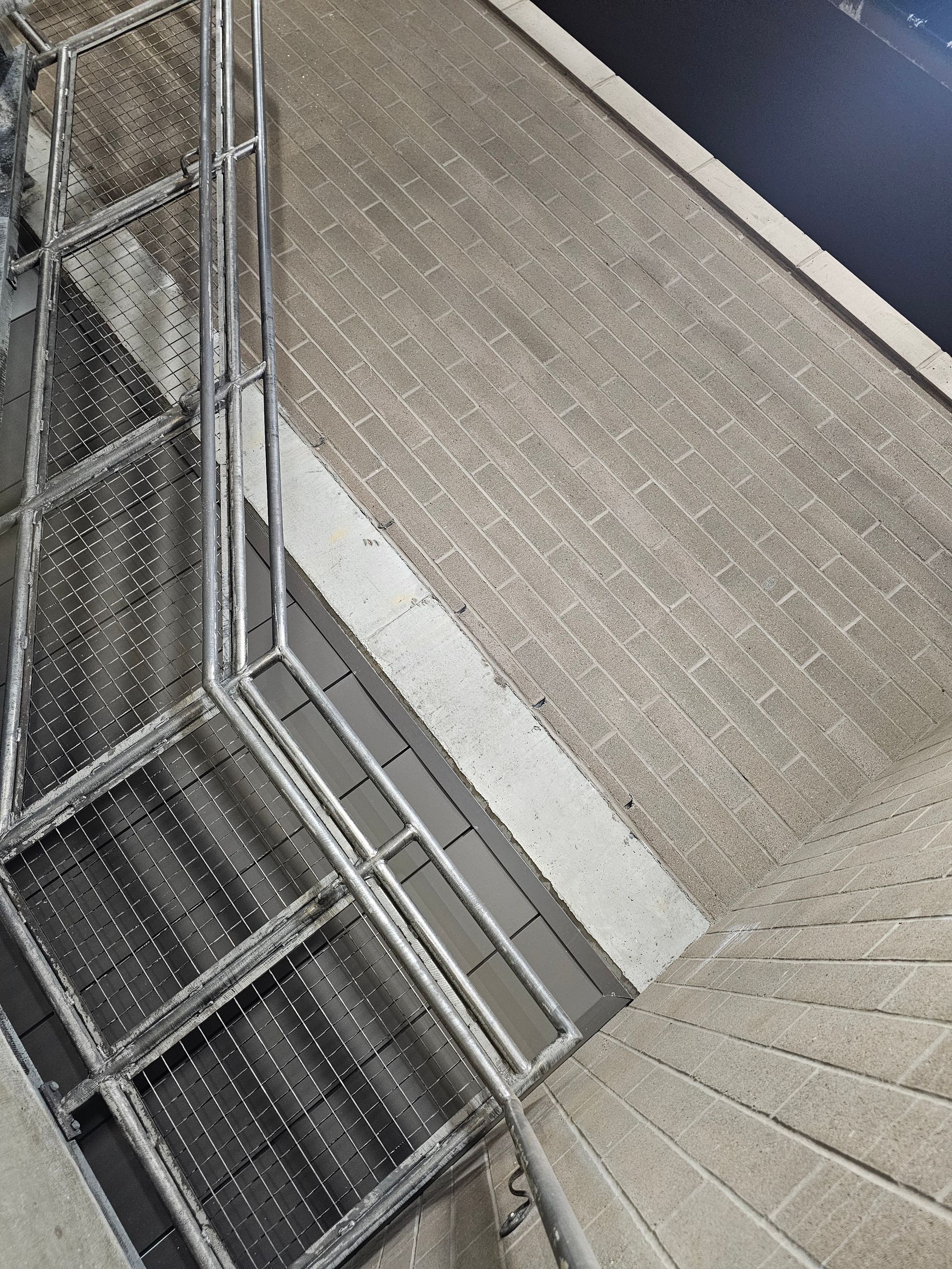 Metal staircase with railing next to a brick wall and a dark surface.