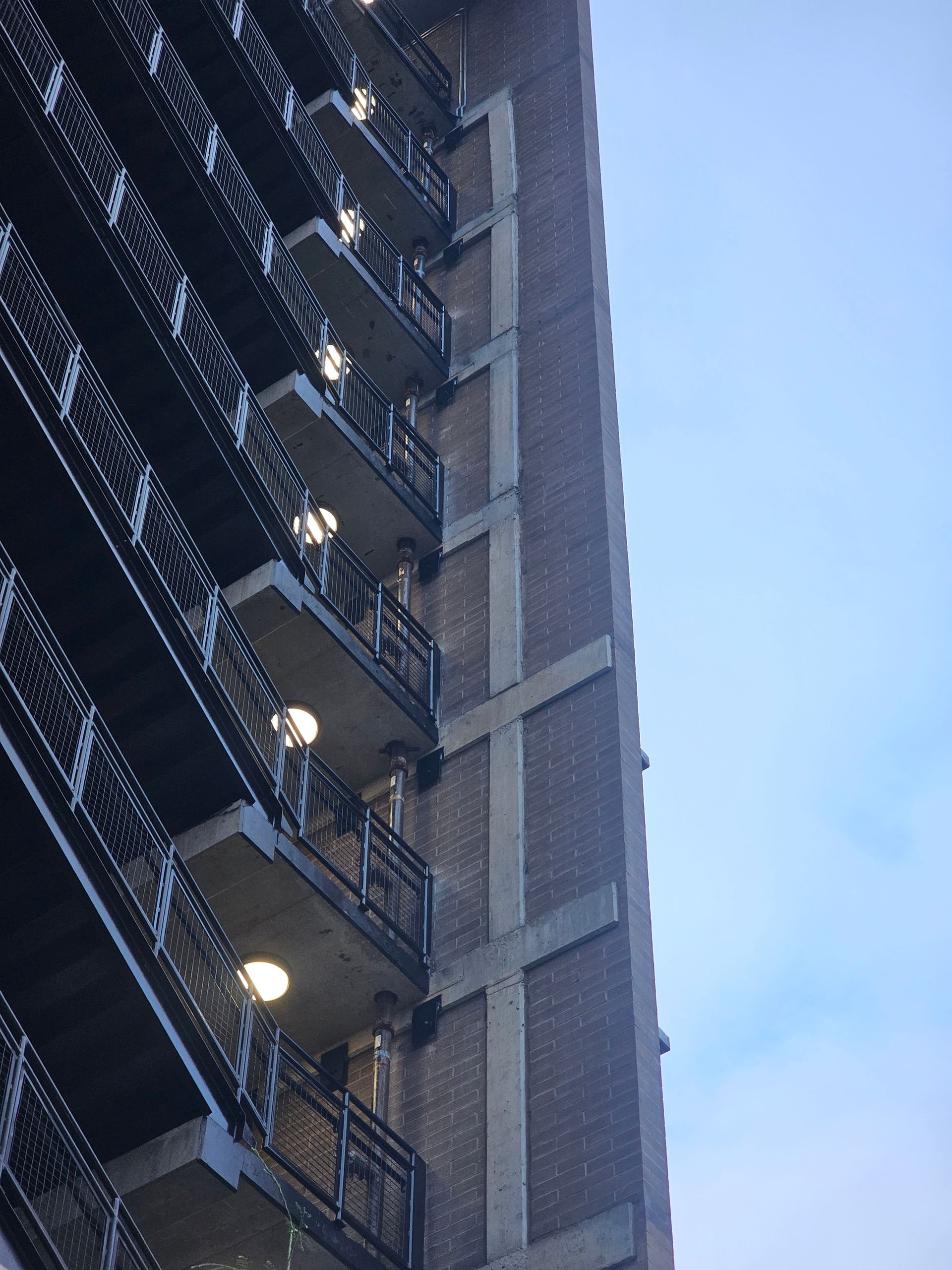 Tall brick building with balconies, partly lit against a blue sky.
