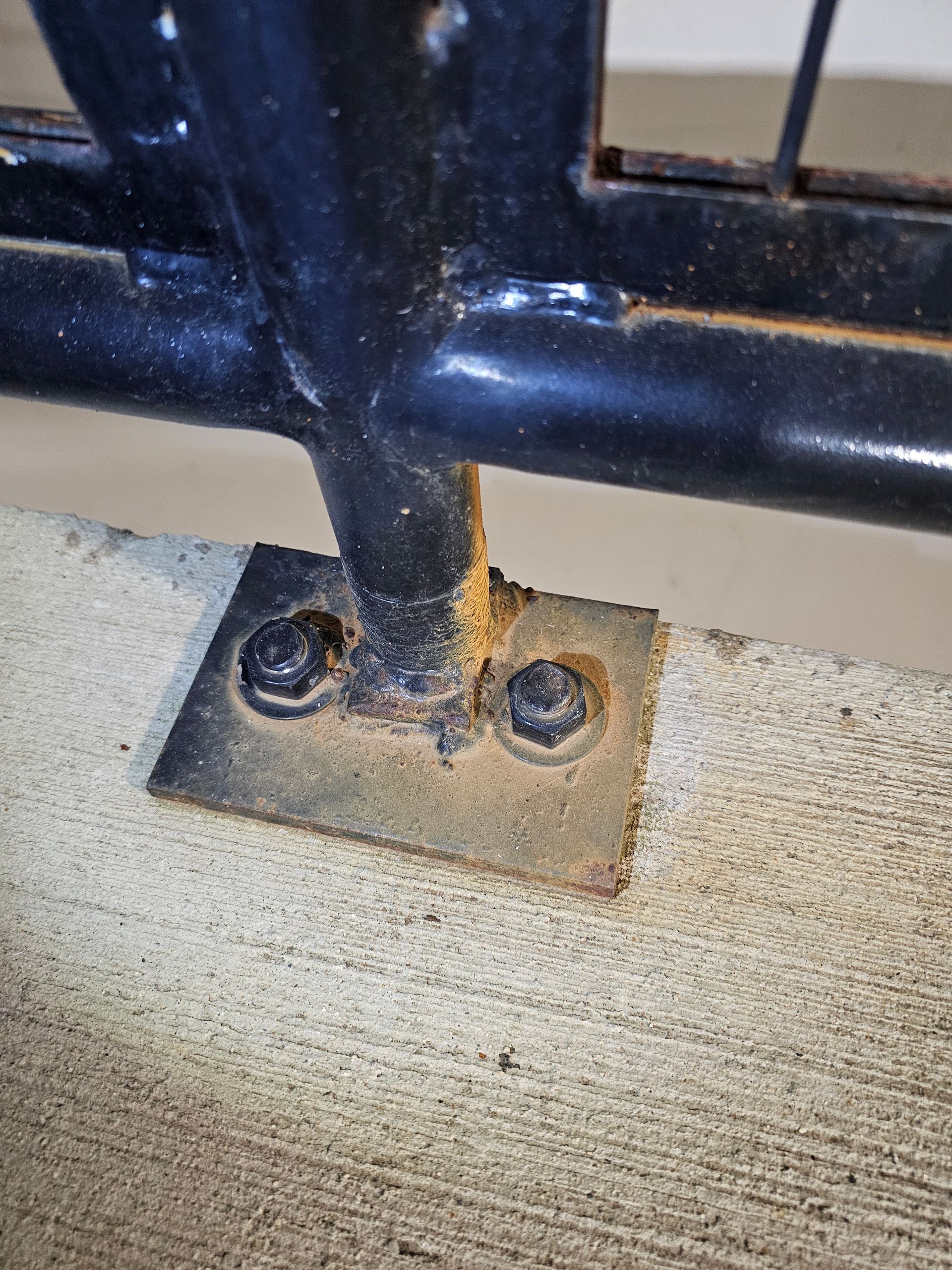 Black metal railing base bolted to a concrete surface, showing rust.