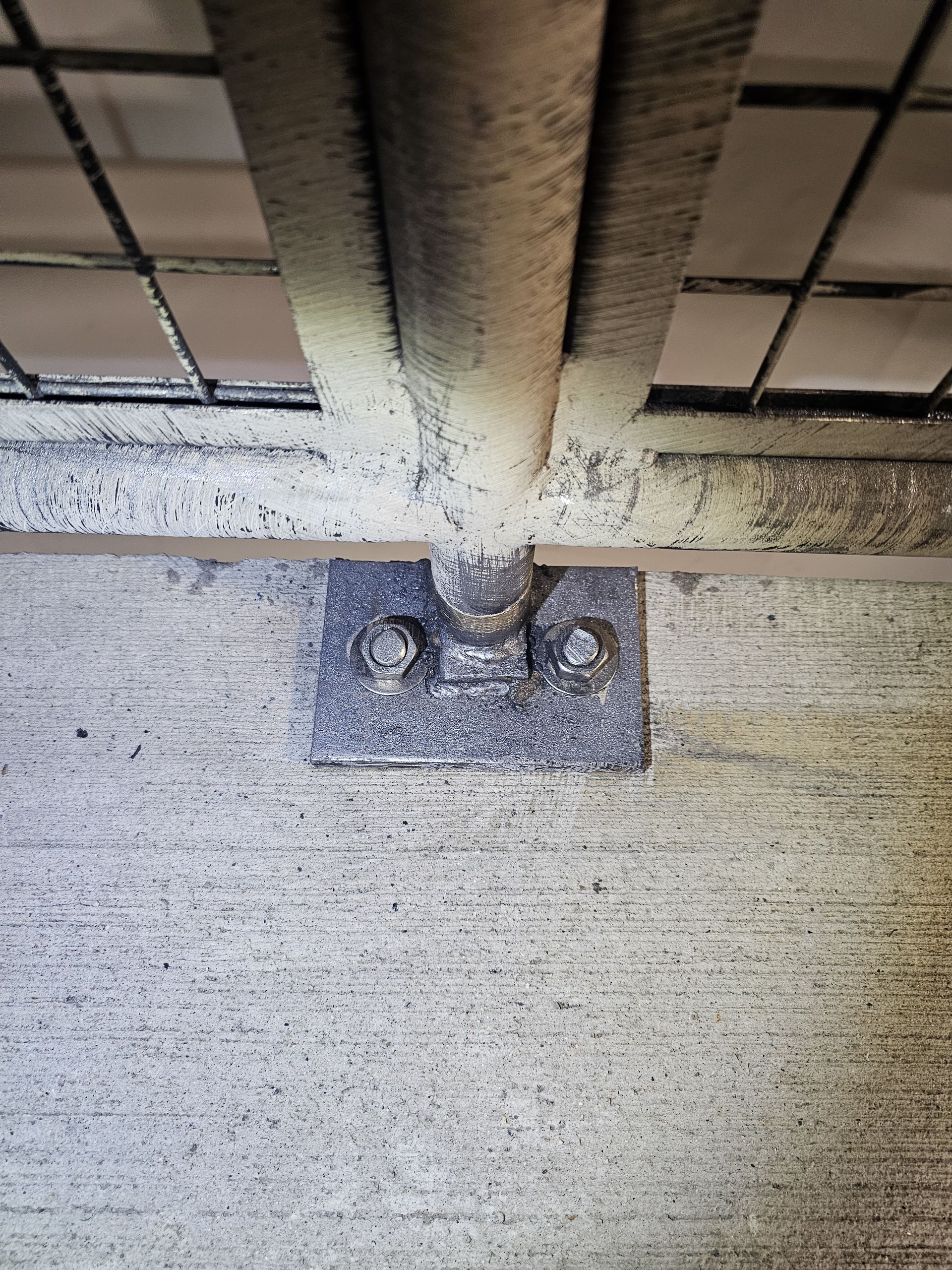 A metal bar and wire mesh attached to a concrete surface with bolts and a bracket.