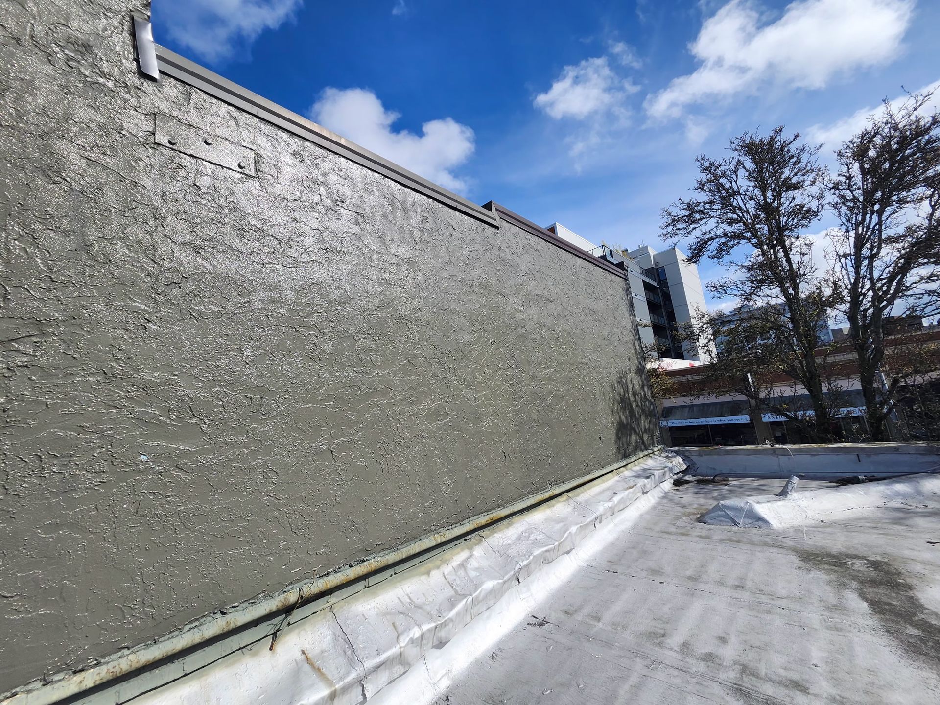 Gray stucco wall against a blue sky, viewed from a rooftop.