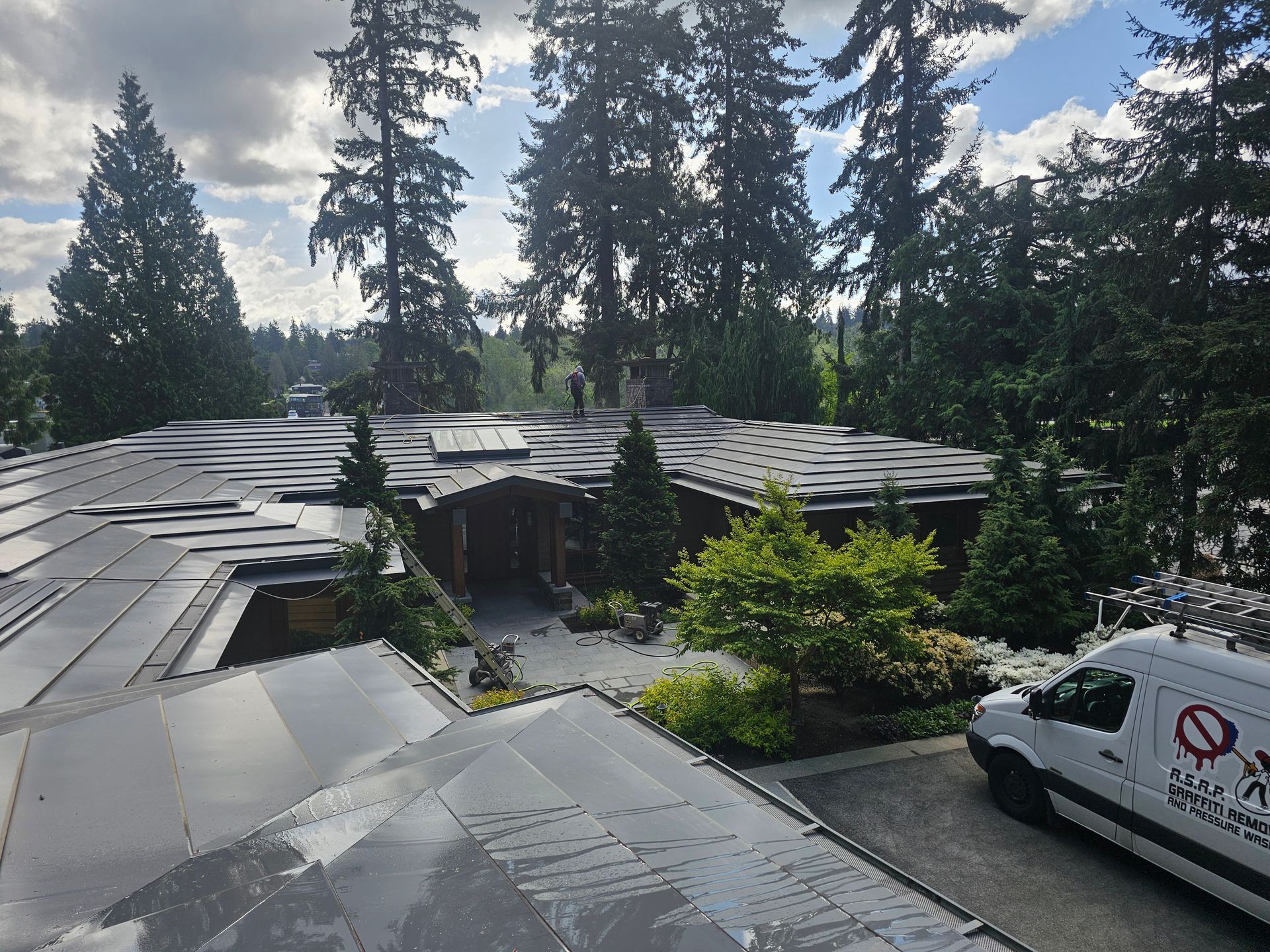 A house with solar panels on the roof, with trees and a van in the yard.