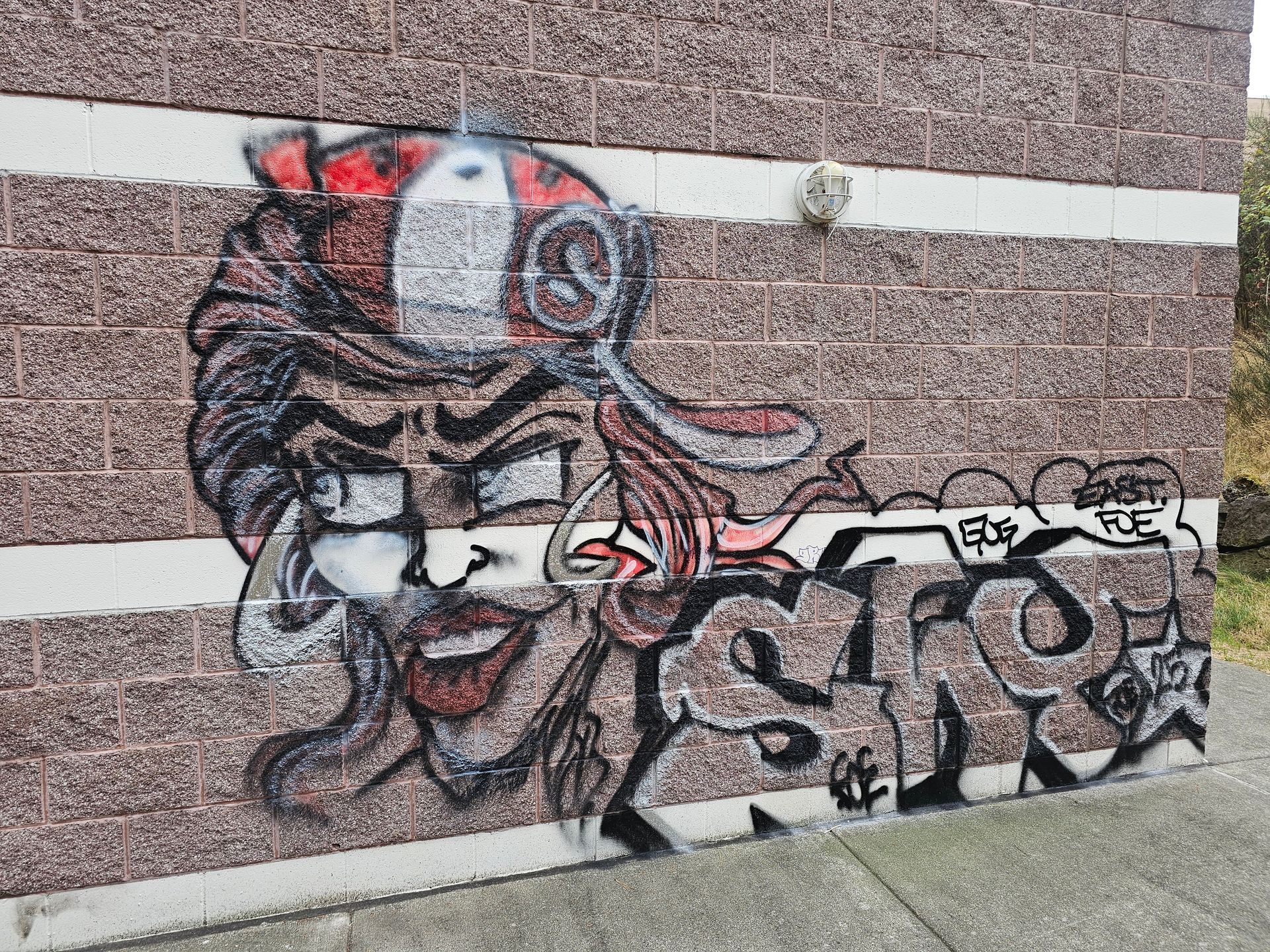 Graffiti of a face and stylized letters on a brick wall; red, black, and white colors.
