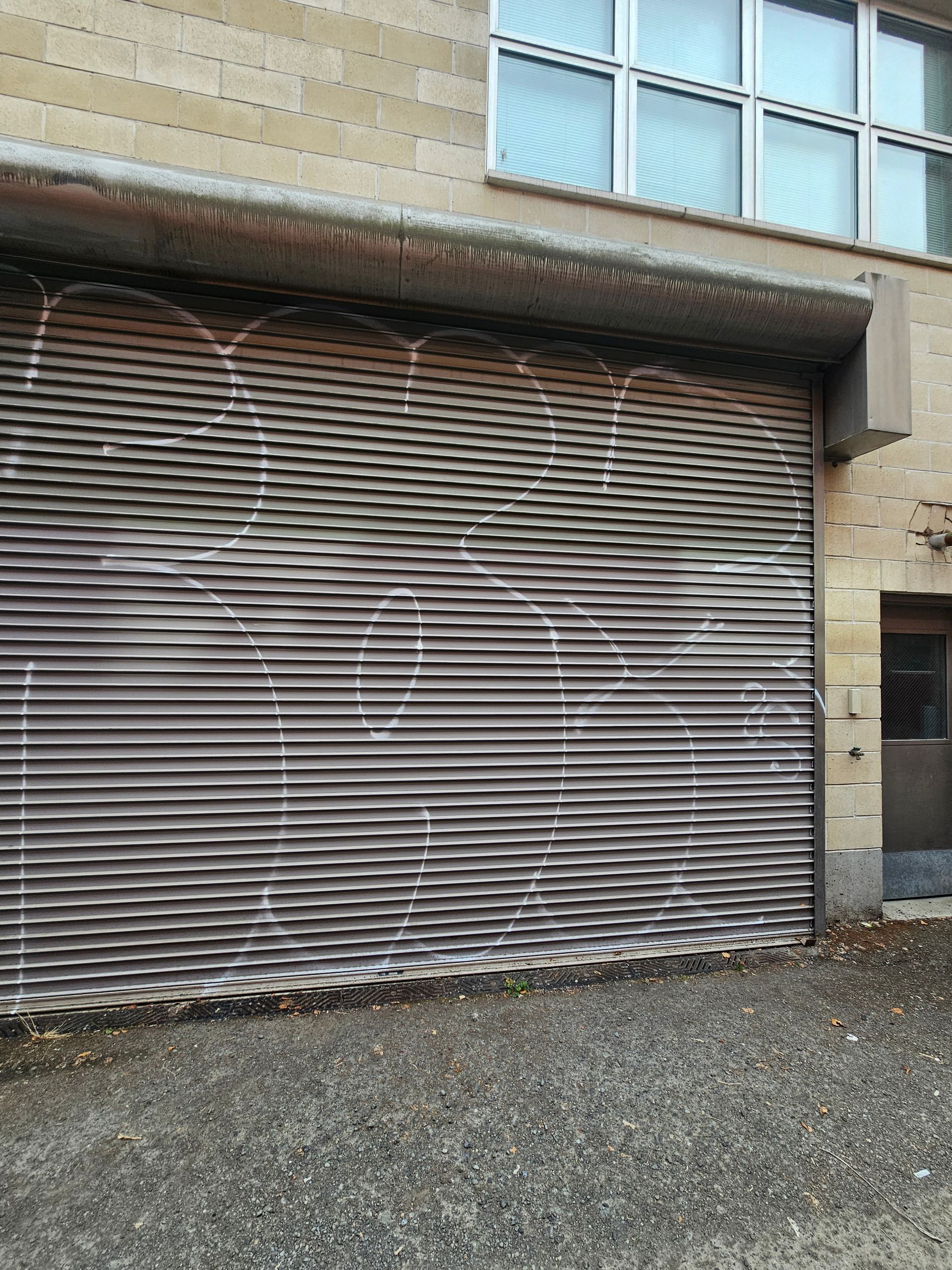 Garage door with graffiti on a building. Gravel path in front.