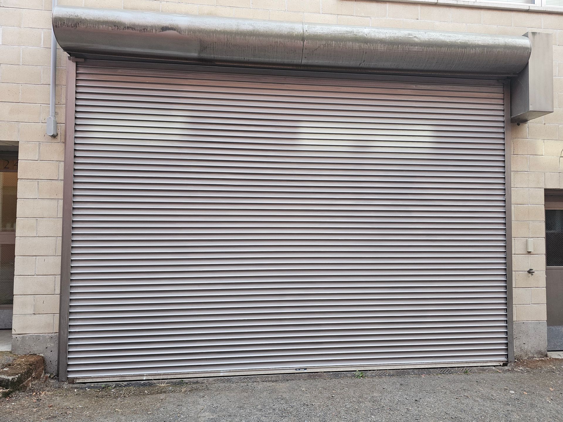Gray metal roll-up door, closed, in a brick building.