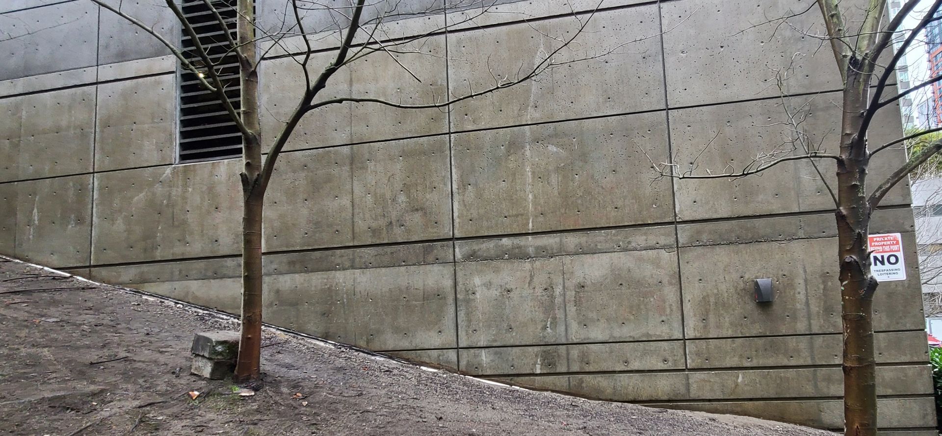 Concrete wall with trees, hillside, and a sign.