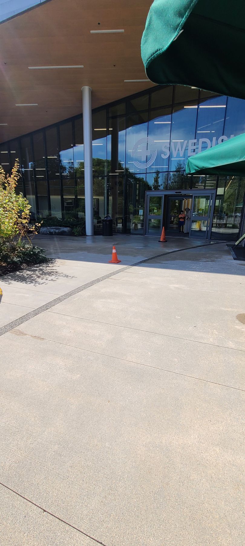 Exterior view of building with glass windows, orange traffic cones, and a green awning.