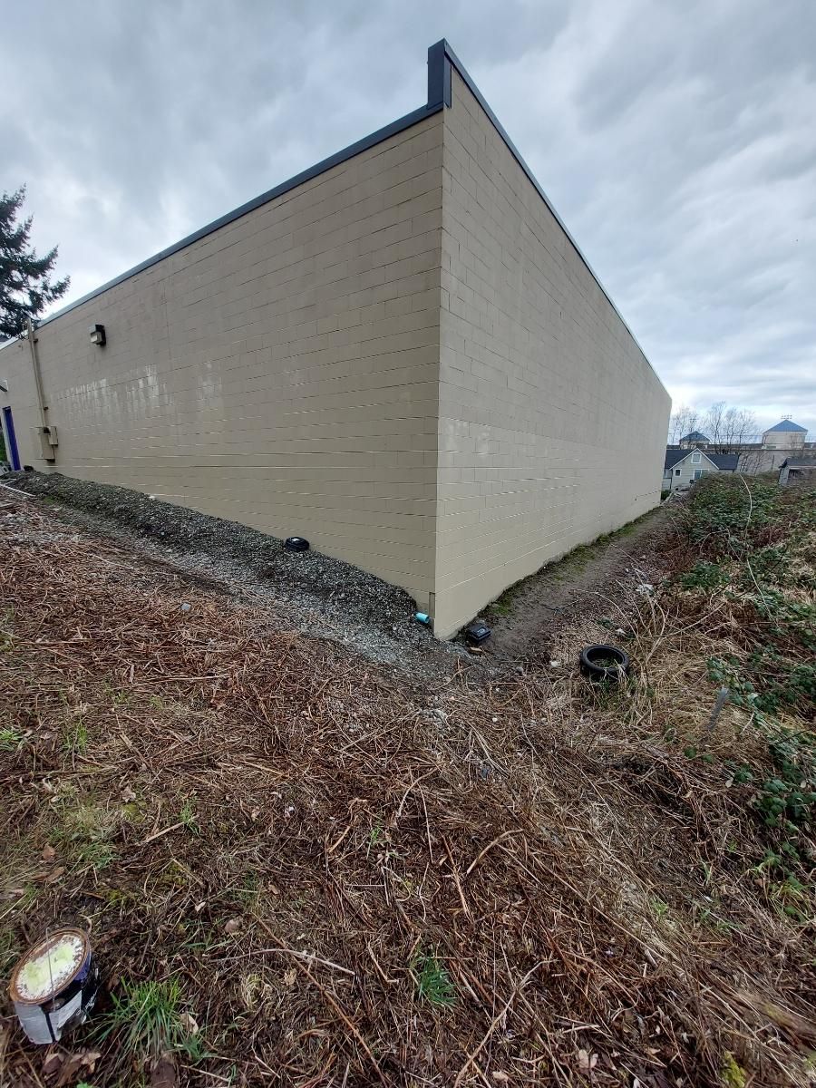 Tan building with black trim, on a hillside covered in brown foliage. Overcast sky.