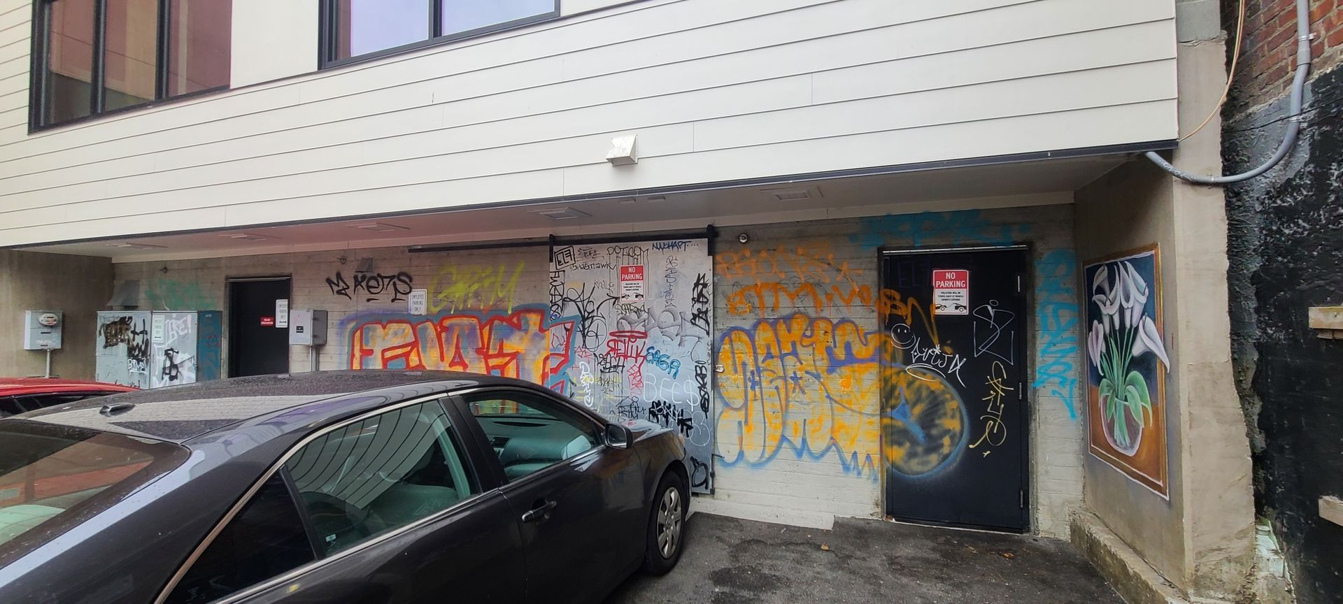 An alley with a car parked in front of a building covered in graffiti art.