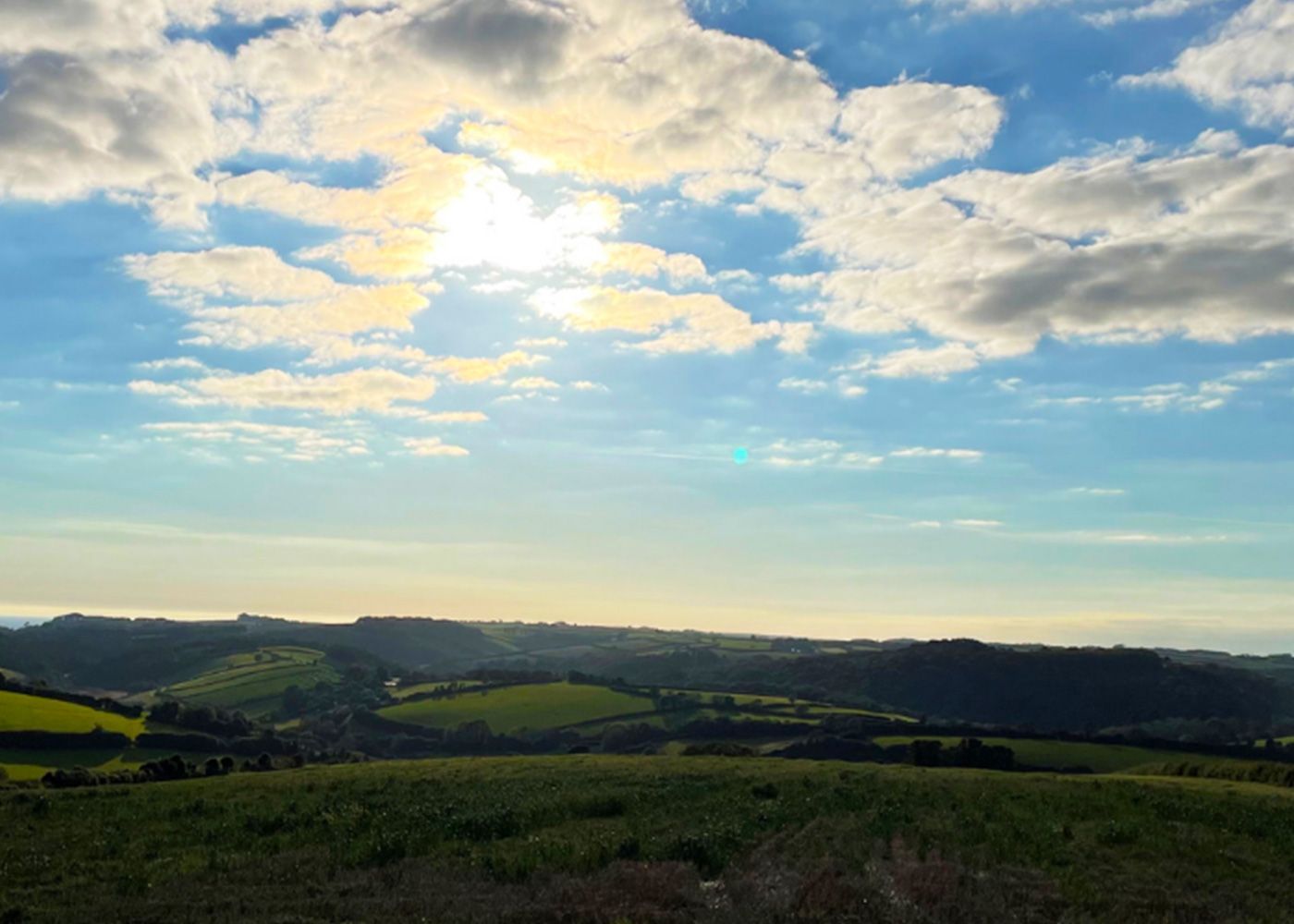 The sun is shining through the clouds over a grassy hillside.