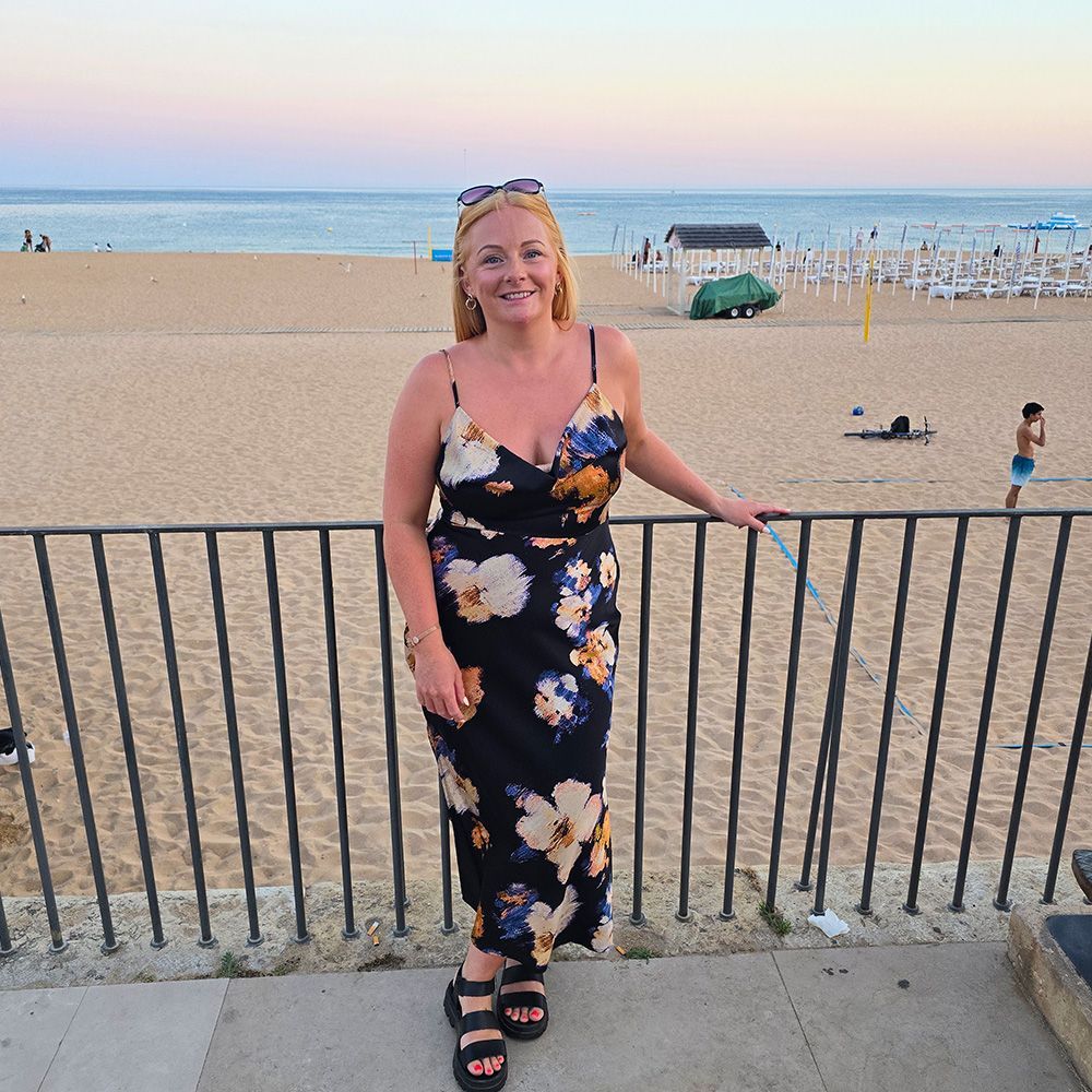 A woman in a floral dress stands in front of a beach
