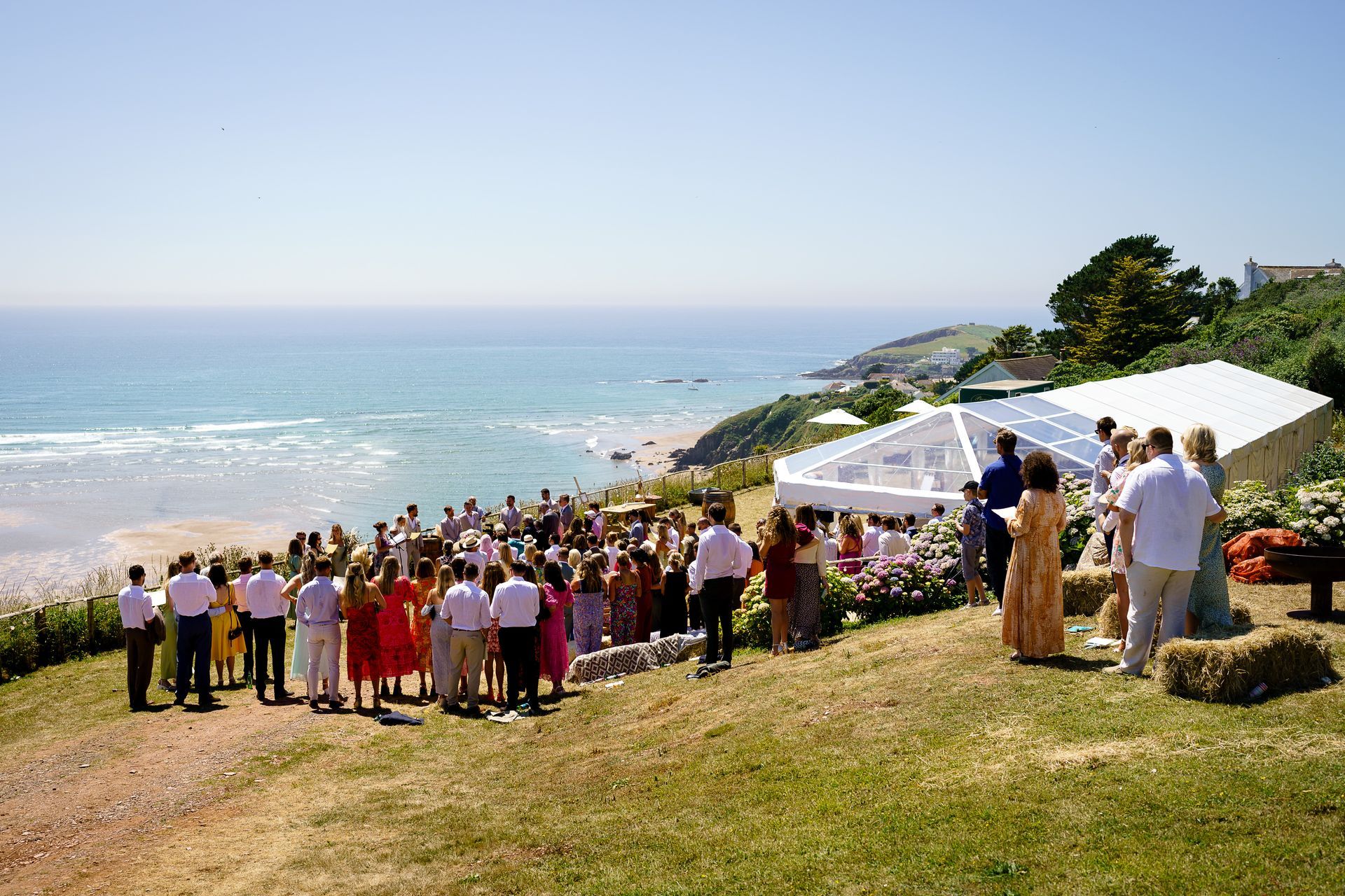 A large group of people are standing in a field under a tent.