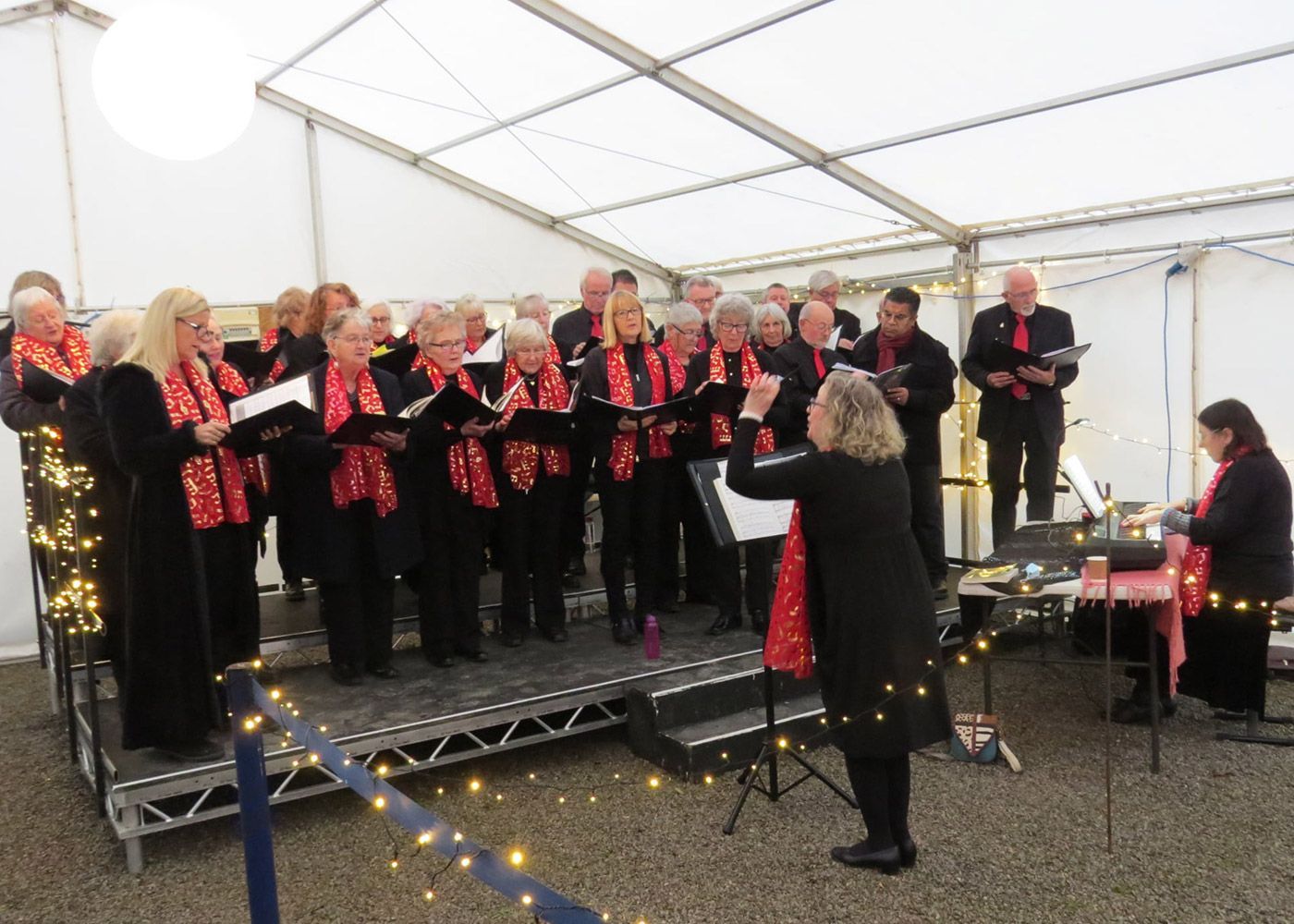A choir is singing on a stage under a tent.